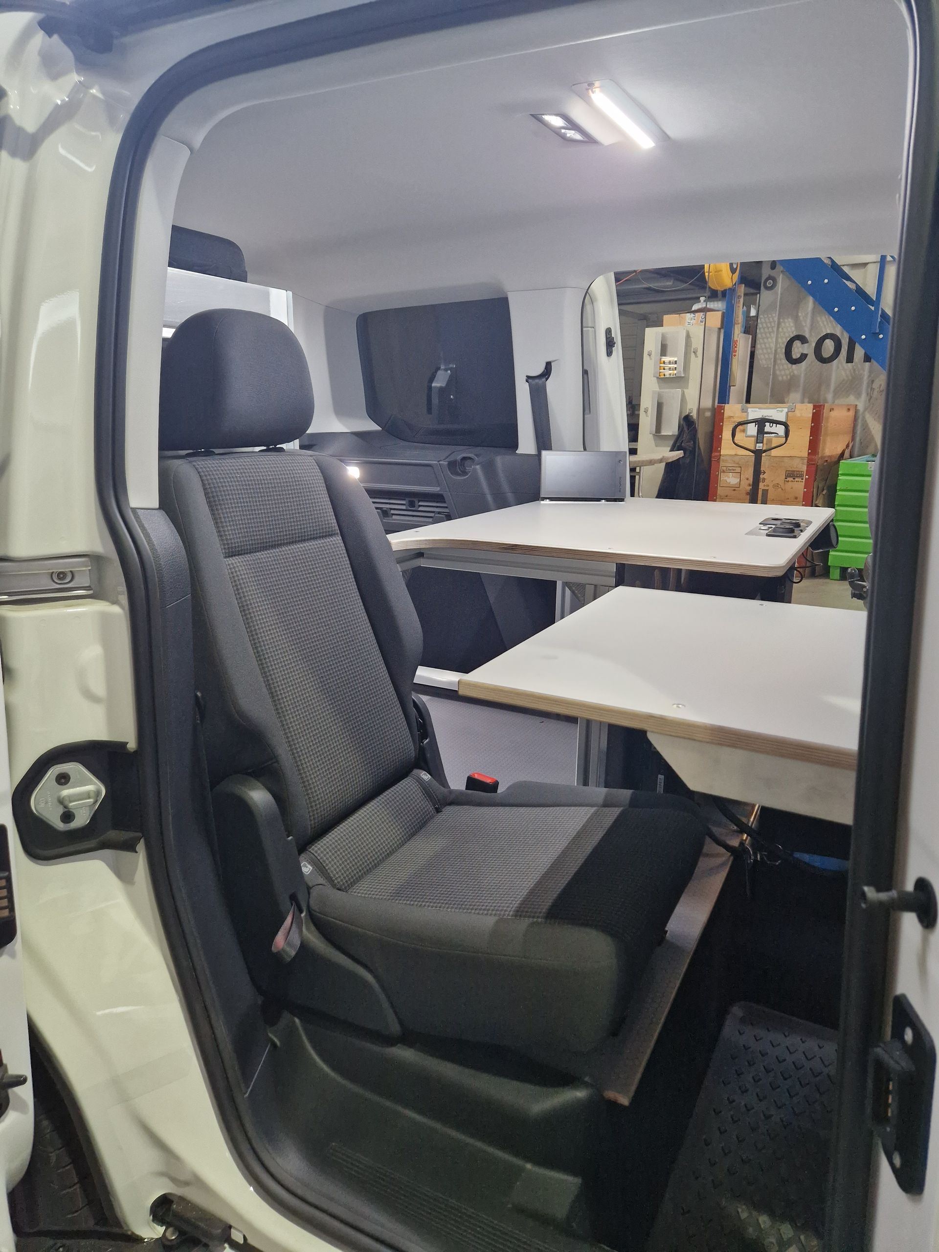 Weißer Van-Innenraum mit einem Sitz und zwei Klapptischen, möglicherweise für Barrierefreiheit modifiziert.