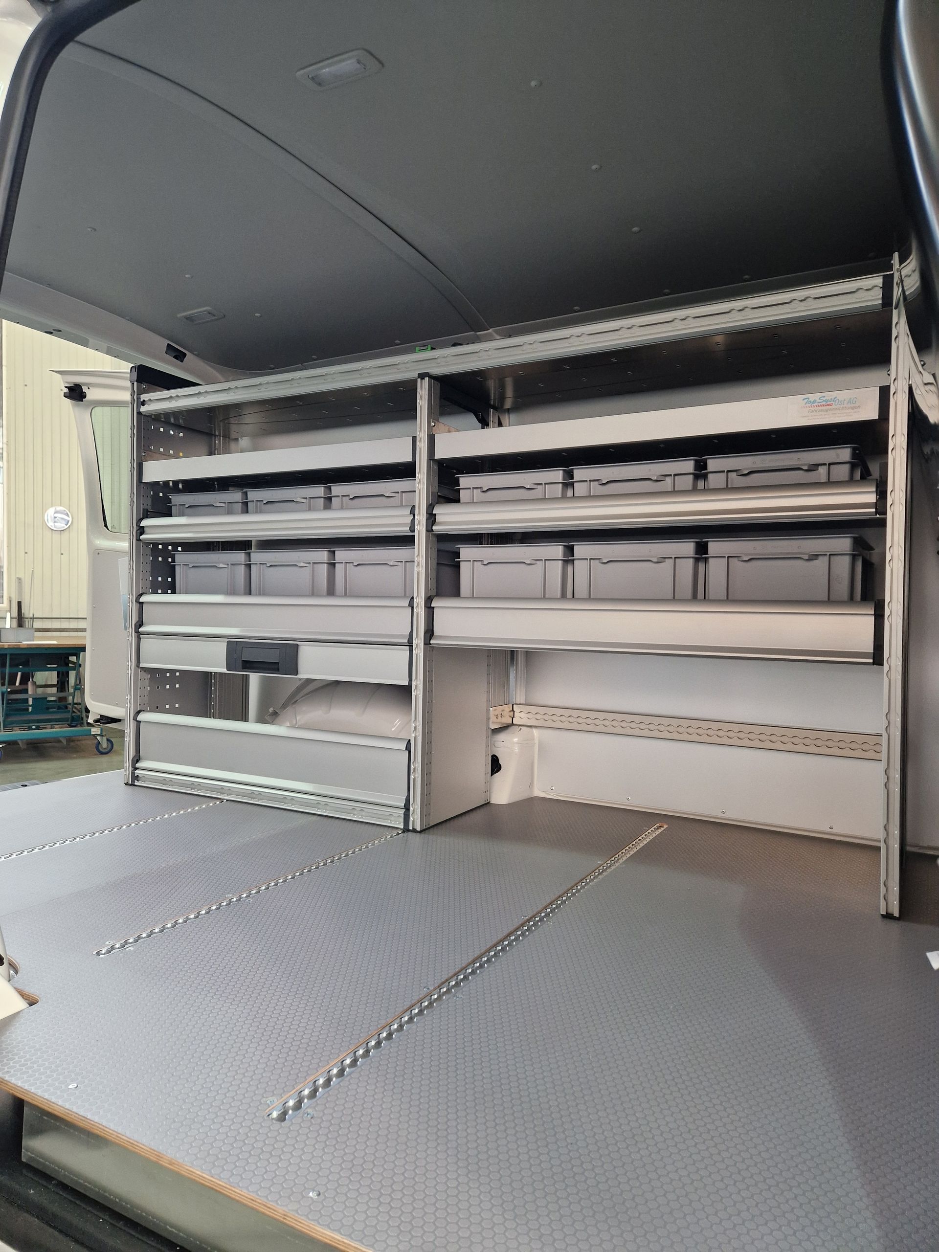 Innenraum eines Lieferwagens mit Regalen, Schubladen und grauen Lagerbehältern.