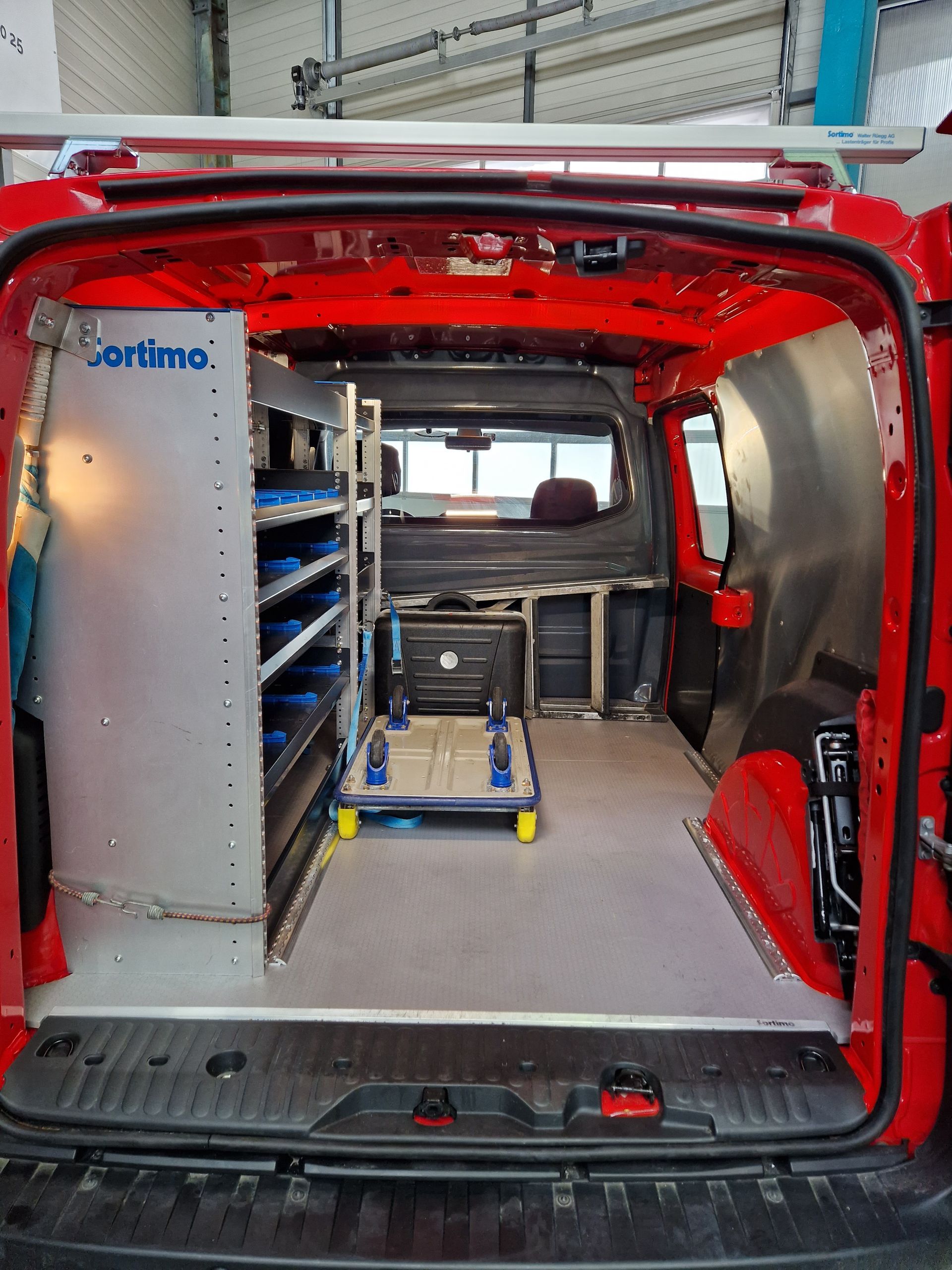 Innenraum eines roten Lieferwagens mit Lagerregalen, Ausrüstung und grauem Bodenbelag.