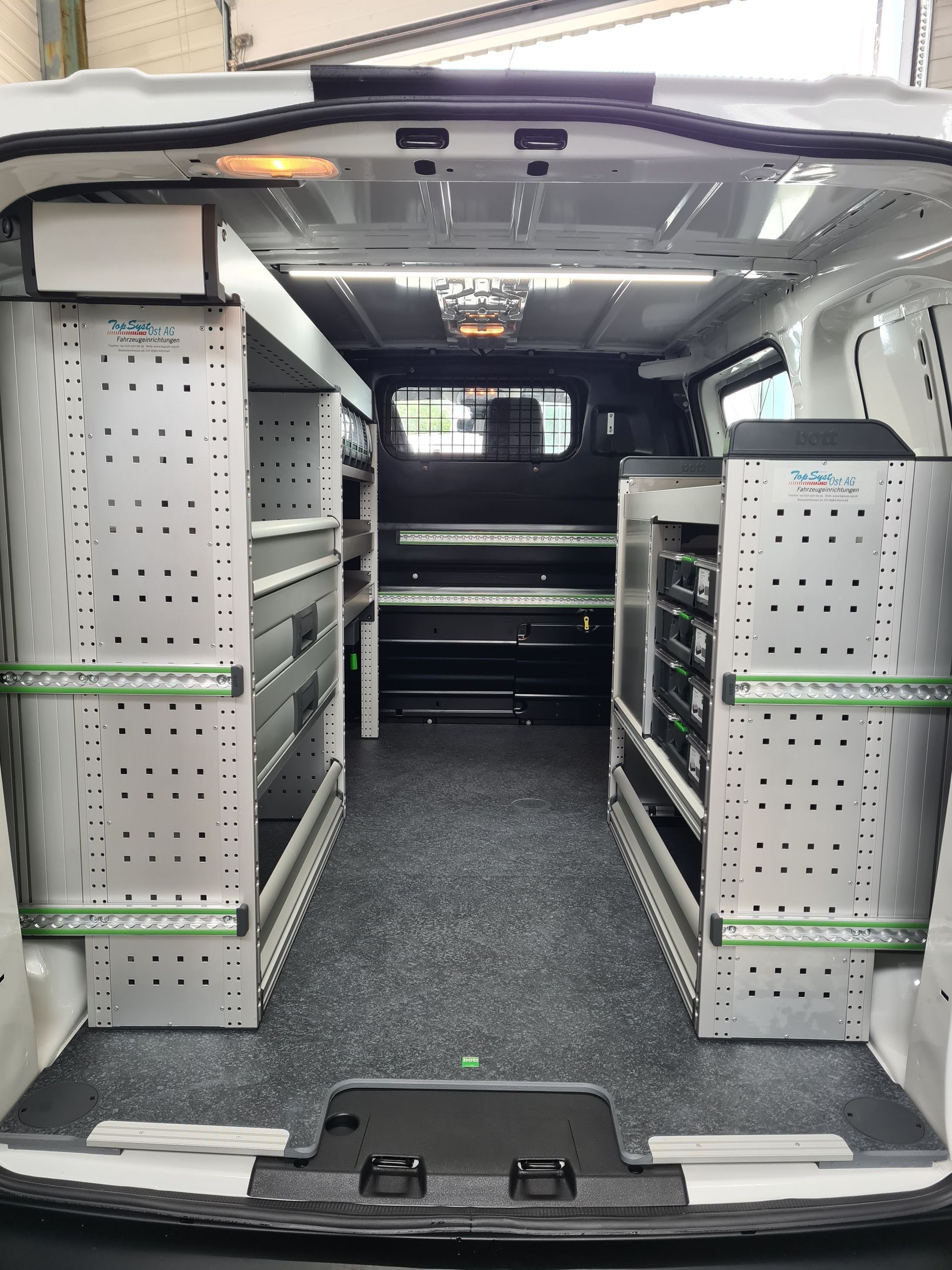 Innenraum eines weißen Lieferwagens mit Regalen und Lagereinheiten, organisiert für Werkzeuge. Schwarzer Boden, weiße Wände und helle Deckenbeleuchtung.