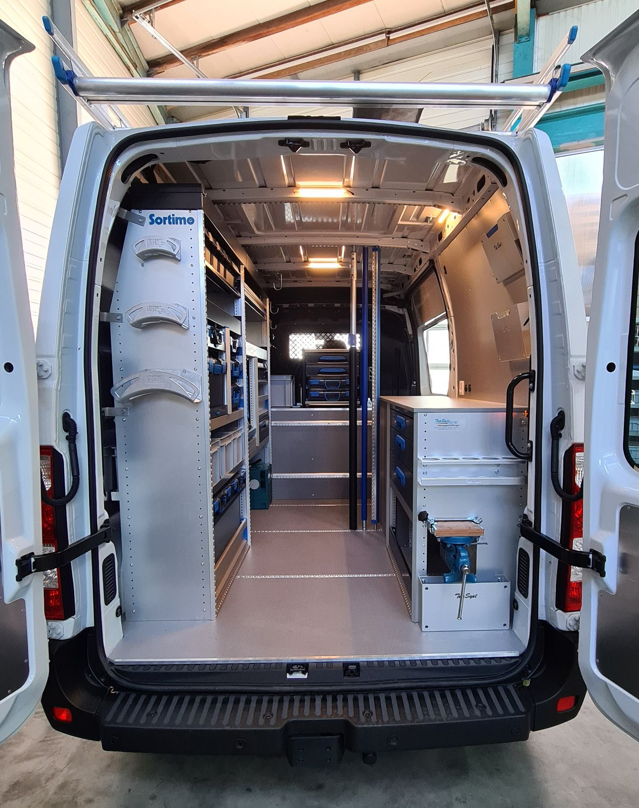 Innenansicht eines weißen Arbeitstransporters mit Regalen und Werkzeugaufbewahrung; die Türen sind geöffnet.