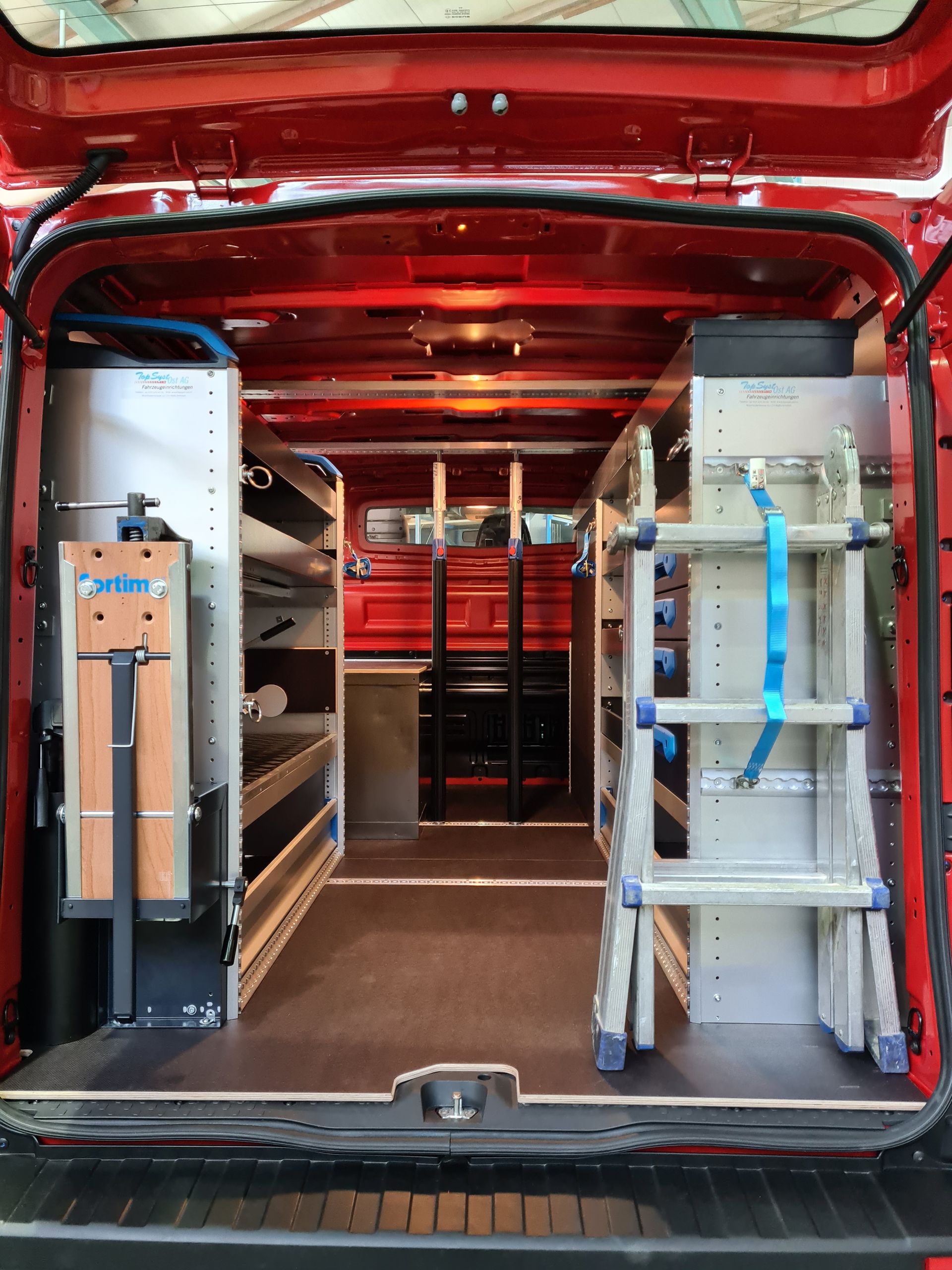 Innenraum eines roten Lieferwagens, ausgestattet mit Regalen, Lagerräumen und einer Leiter für Werkzeuge und Ausrüstung.