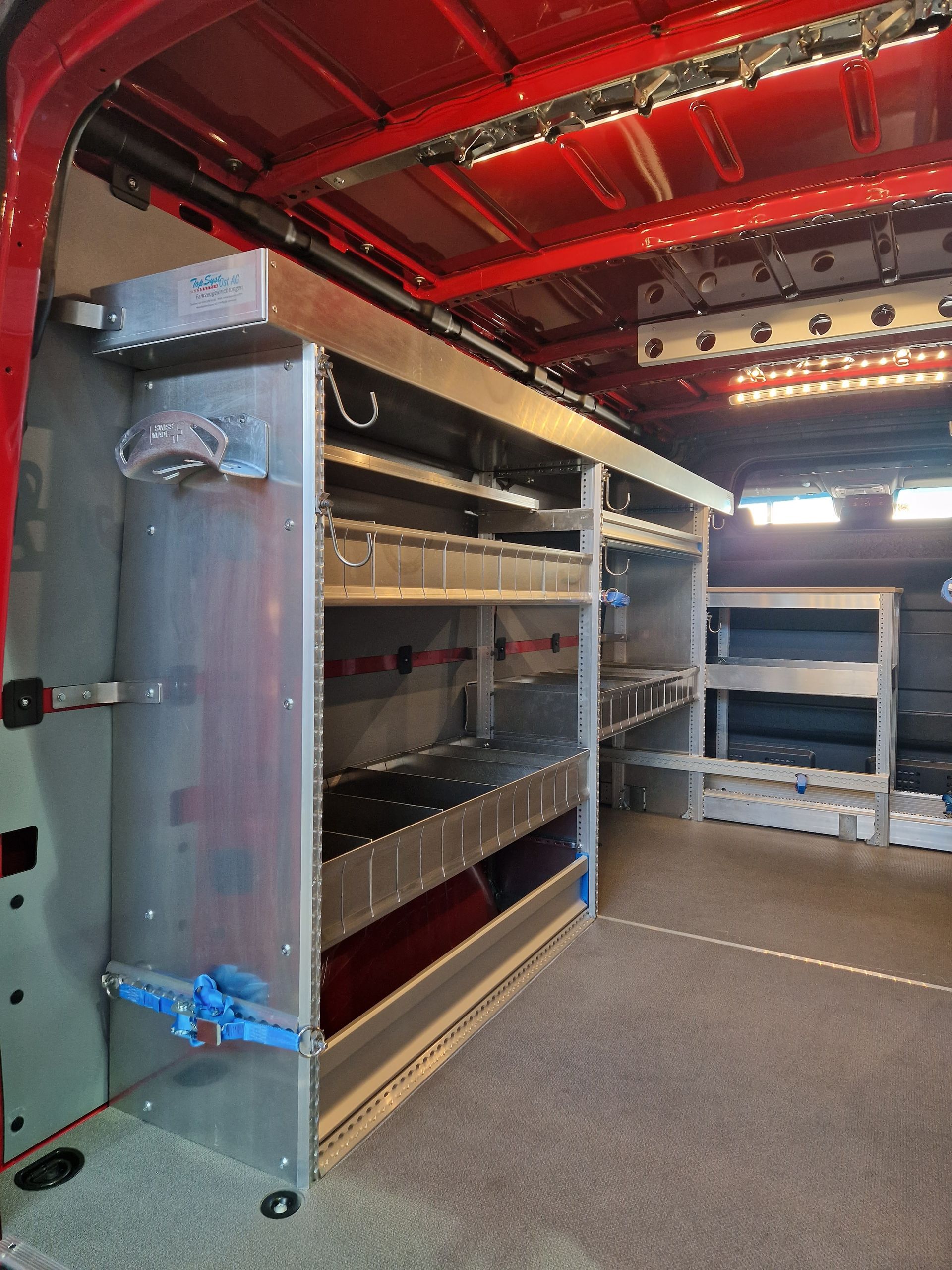 Innenraum eines roten Servicewagens mit Regalen und Fächern zur Aufbewahrung von Ausrüstung, silbernes Metall.