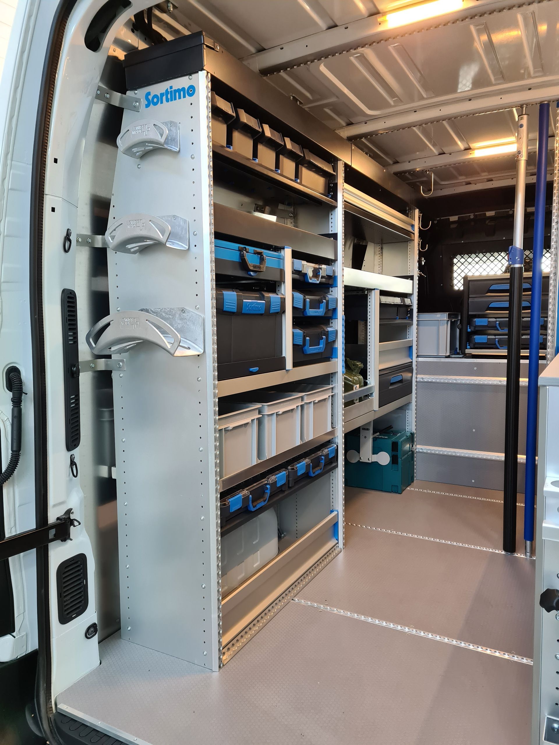 Innenraum eines weißen Lieferwagens mit geordneten Regalen, Behältern und Werkzeugen zur Aufbewahrung, der einen gut organisierten Arbeitsbereich zeigt.