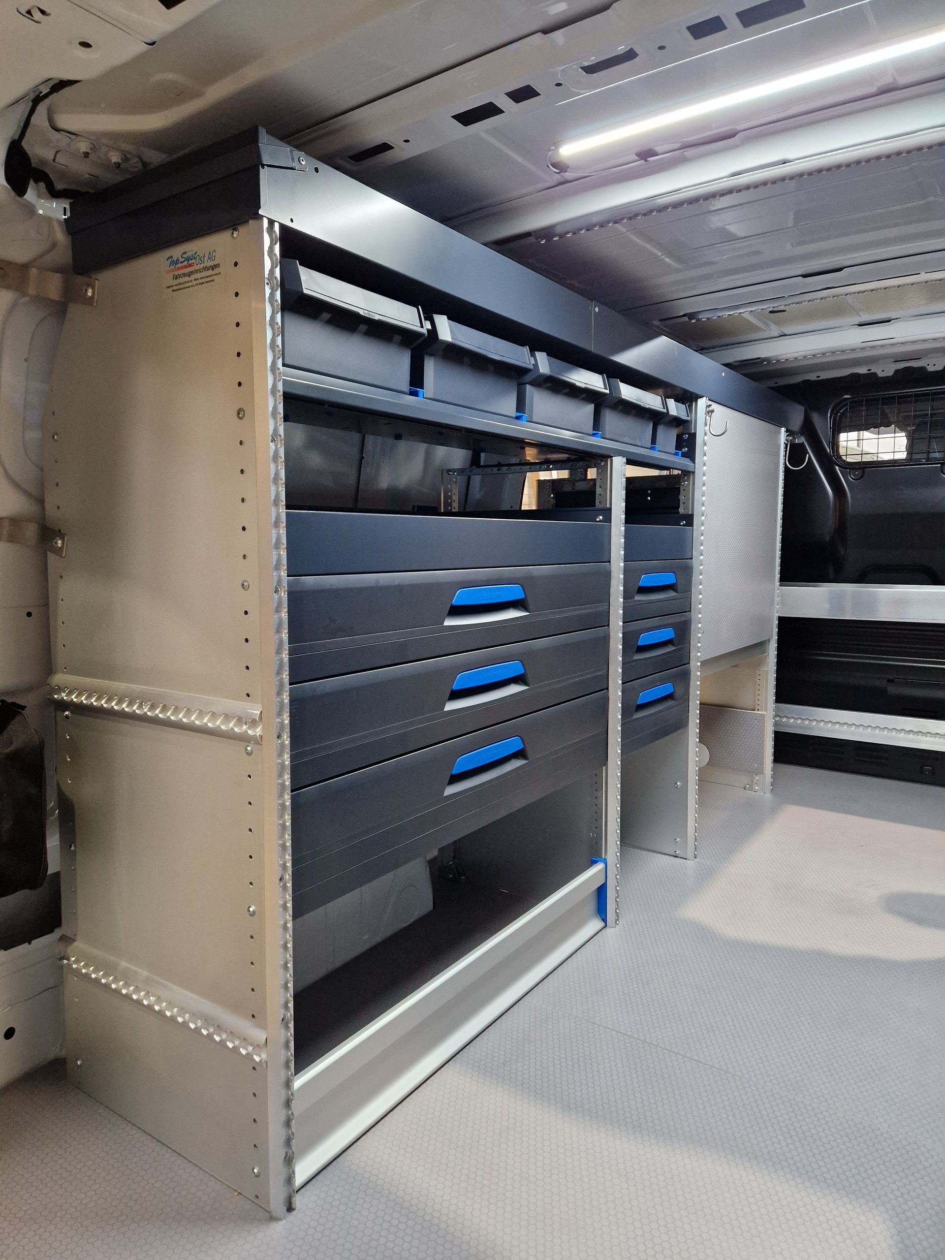 Innenansicht eines Lieferwagens mit maßgefertigten Metallregalen und Schubladen für Werkzeuge und Vorräte; Silber, Schwarz und Blau.
