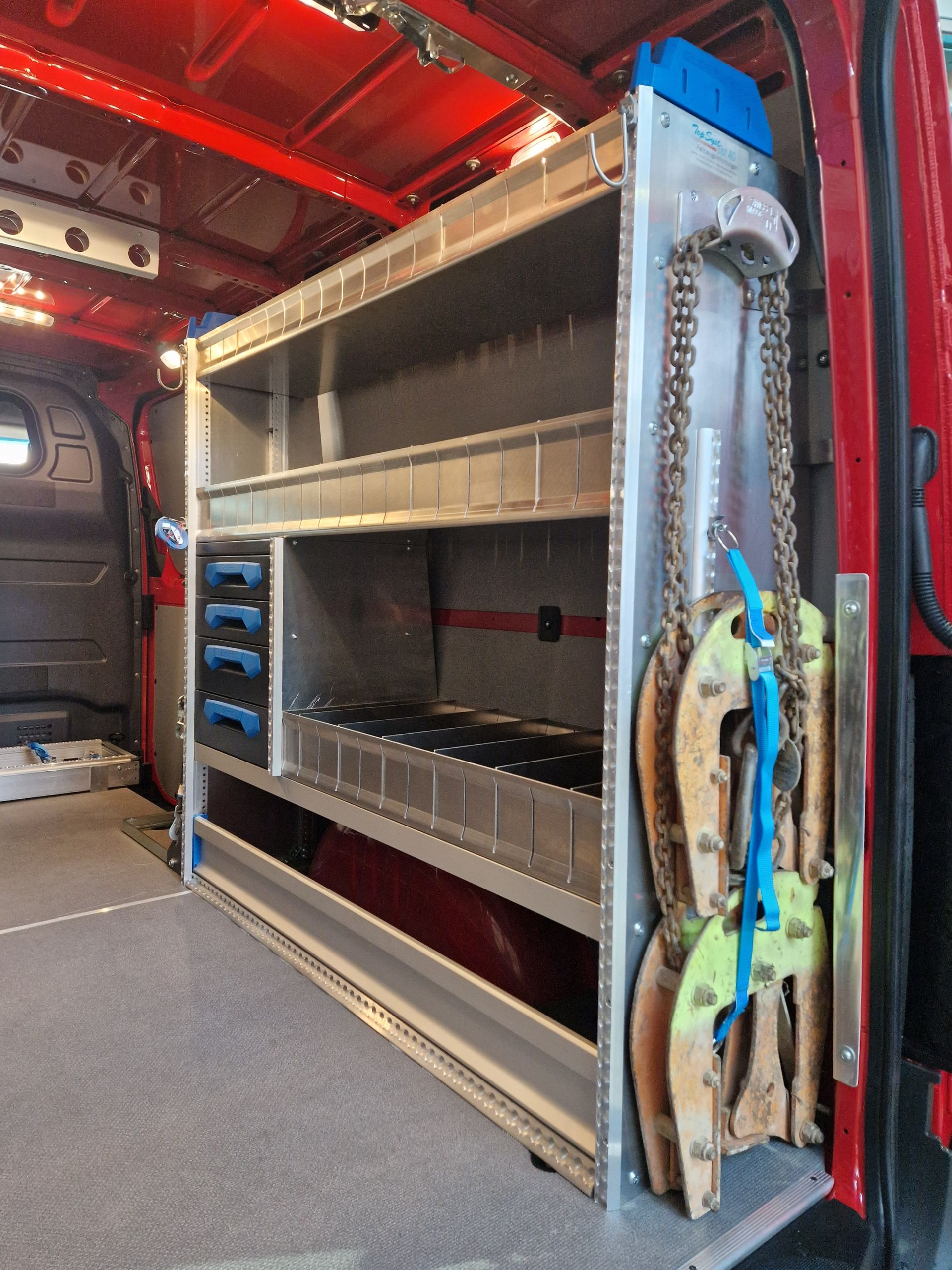 Innenansicht eines roten Lieferwagens mit Regalen für Werkzeuge und Ausrüstung. Ketten und Klammern sind an der Seite gelagert.
