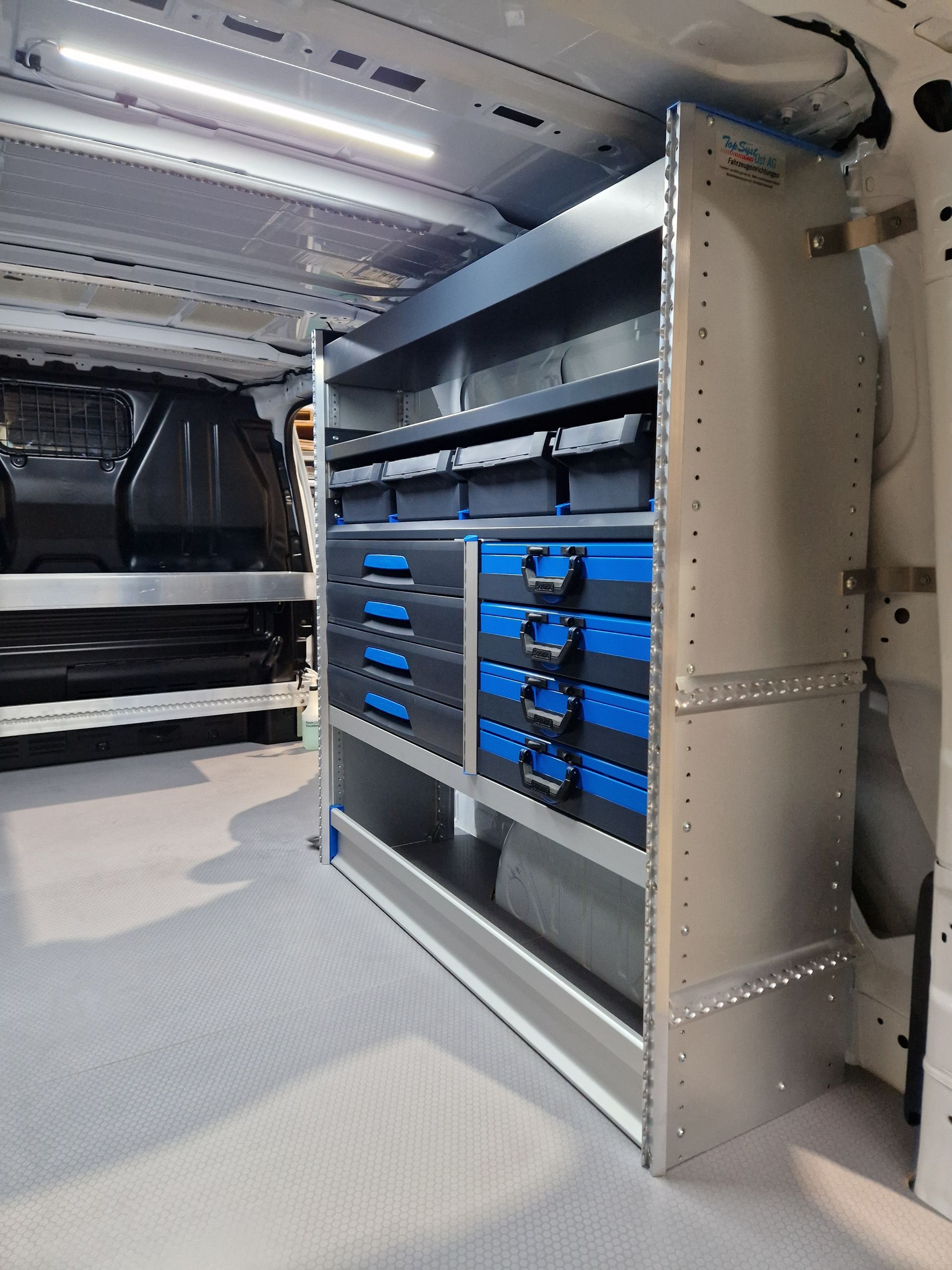 Innenansicht des Lieferwagens mit Metallregalen mit blauen und schwarzen Schubladen und Behältern.