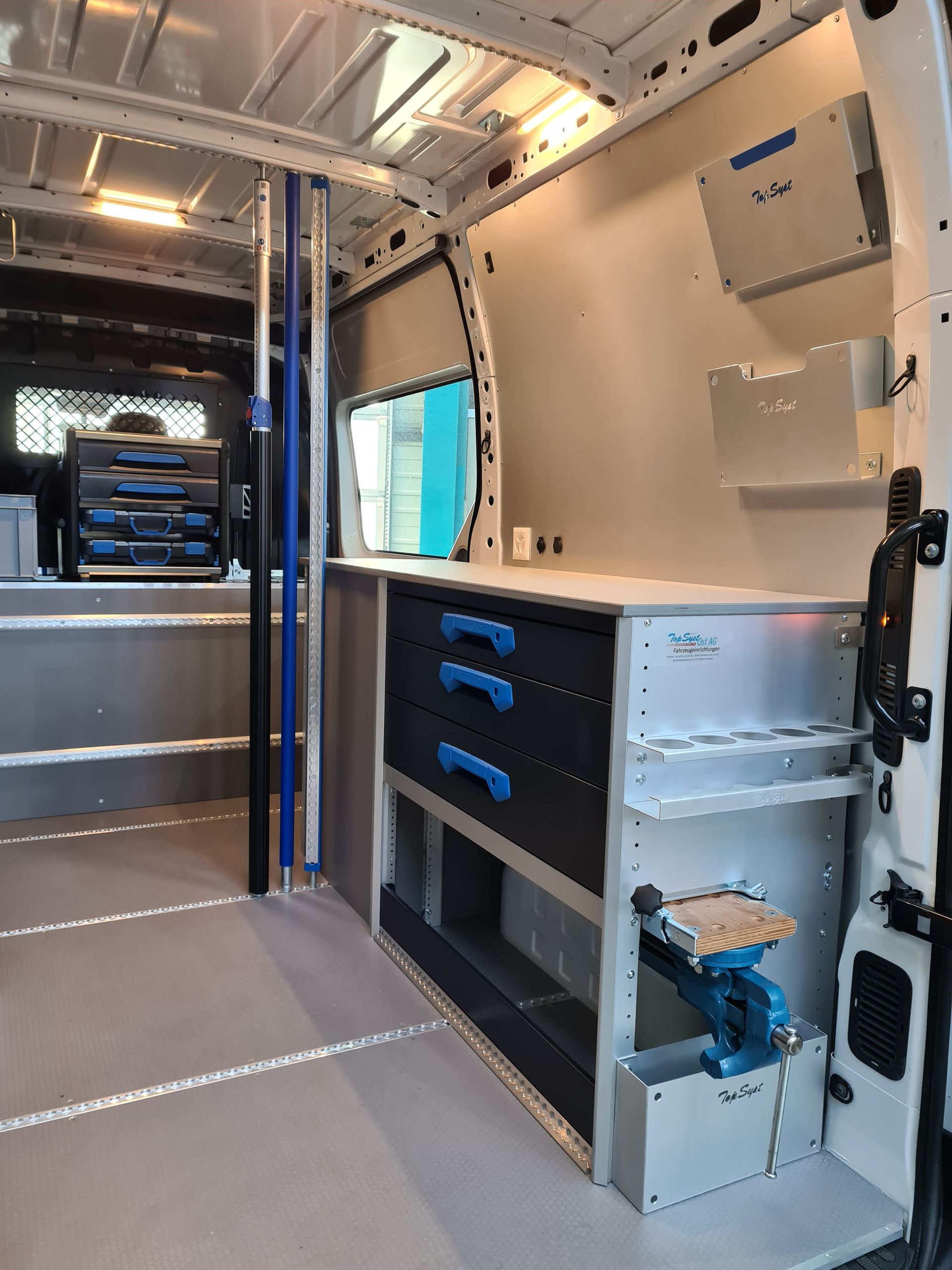 Innenansicht eines Arbeitswagens. Metallregale und Schubladen, ein Schraubstock und Werkzeuge sind sichtbar.