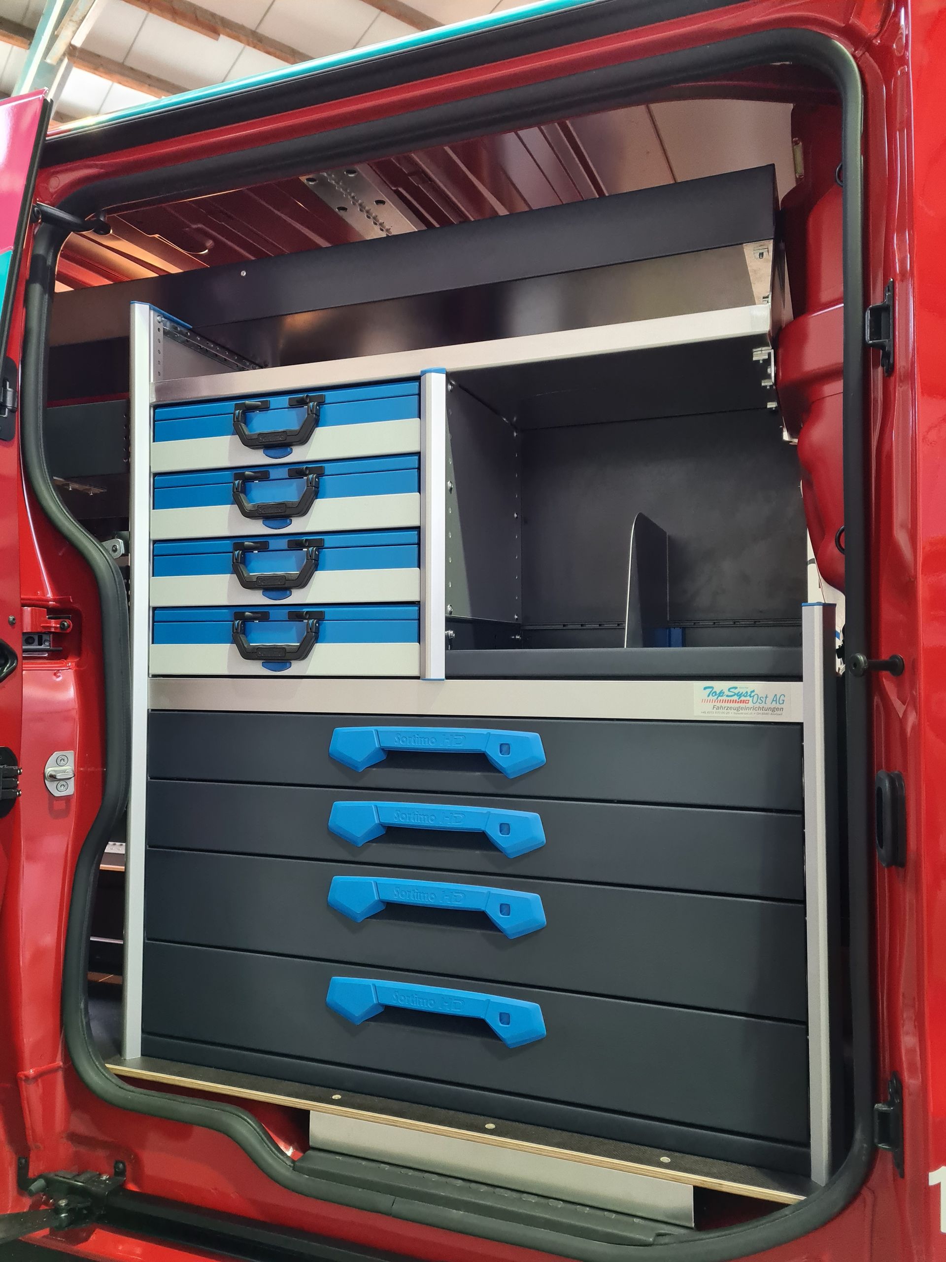 Innenausstattung eines roten Lieferwagens mit Regalen und Schubladen zur Aufbewahrung von Werkzeugen.