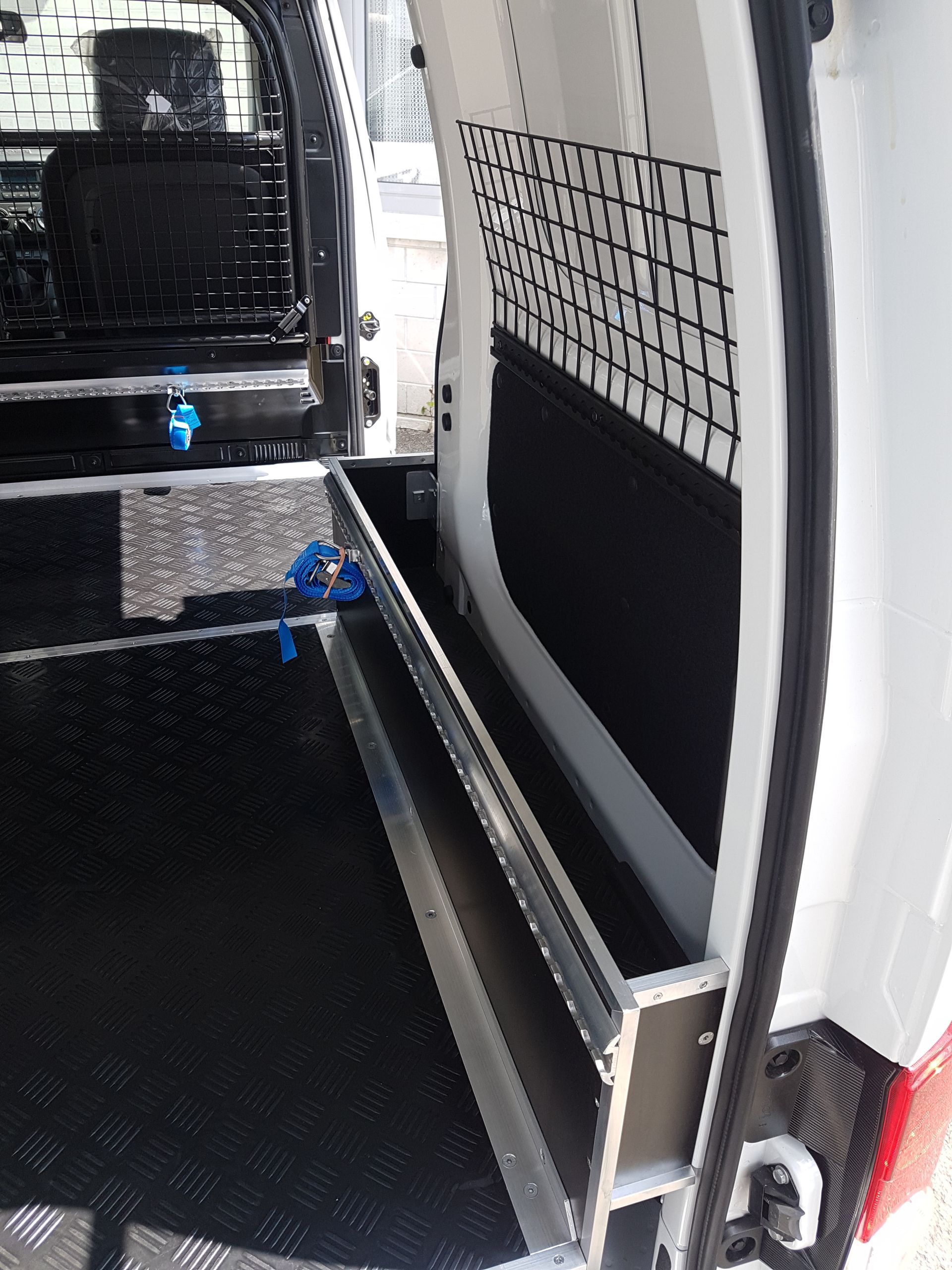 Innenraum eines weißen Lieferwagens mit Staufächern, schwarzem Rautenplattenboden und Netzgewebe.