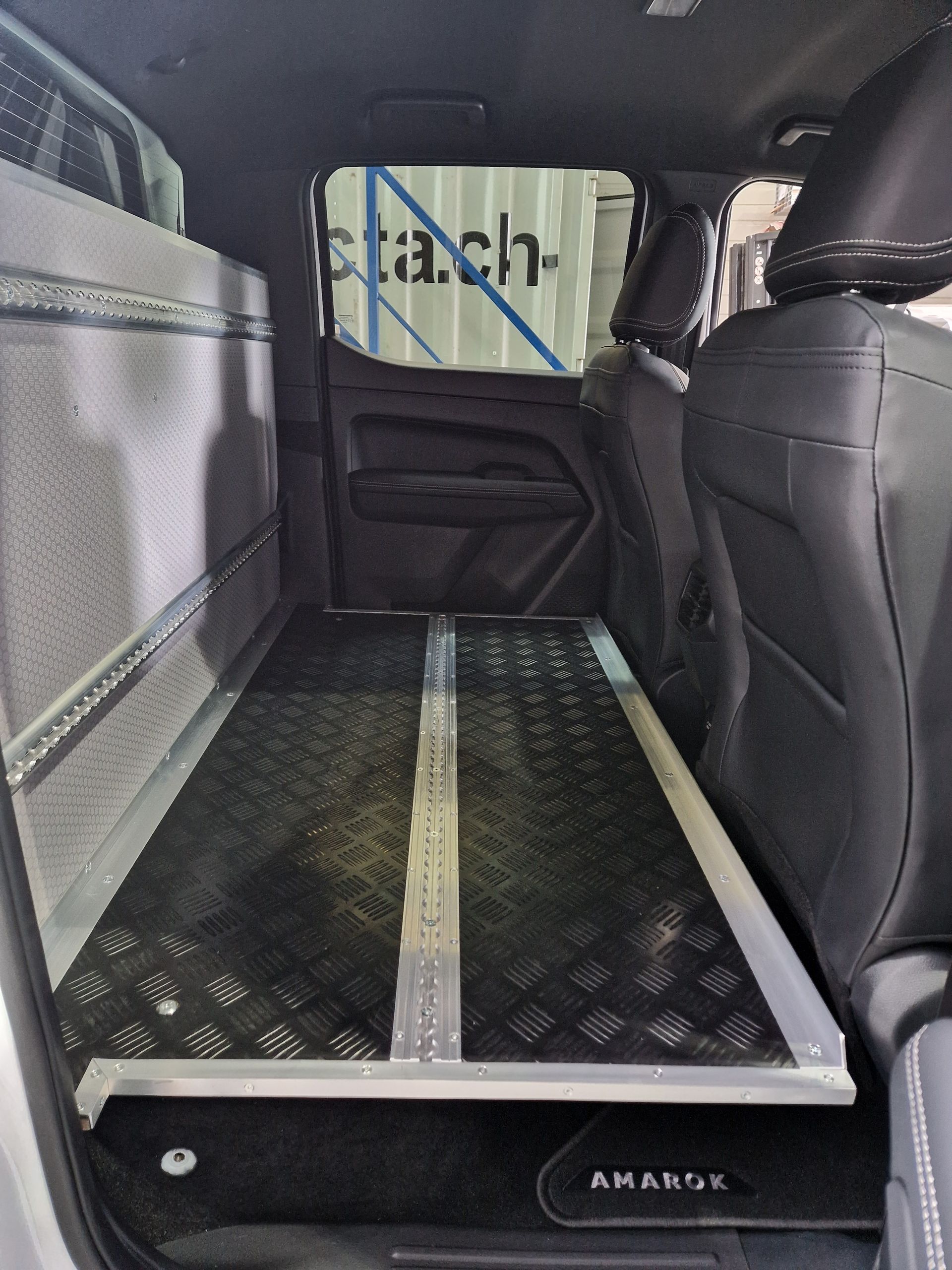 Innenraum eines LKW mit ausziehbarer schwarz-silberner Ladefläche. Rechts sind die Sitze zu sehen.