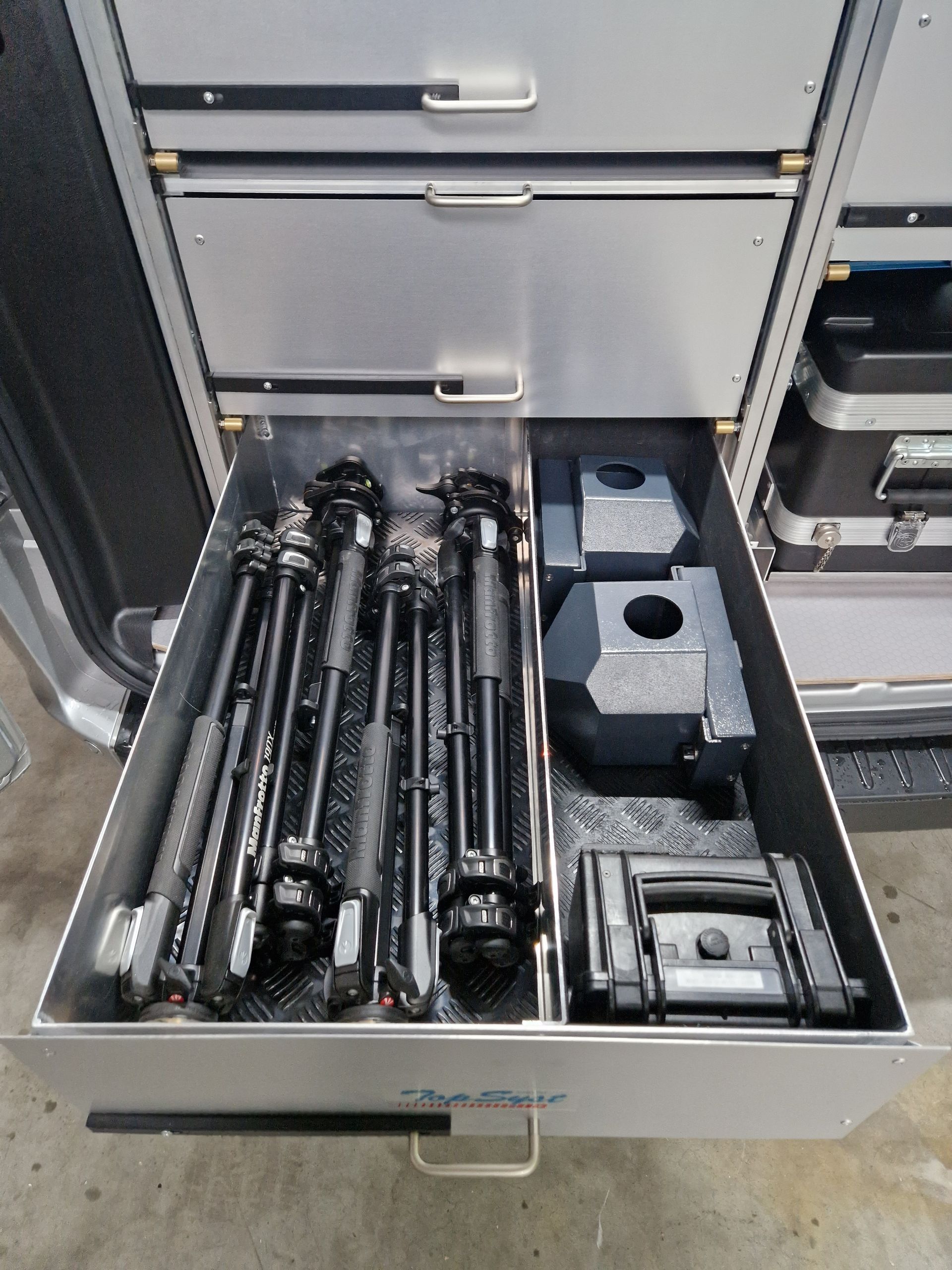 Schublade in einem Metallschrank mit Stativen, Gewichten und anderer Ausrüstung.