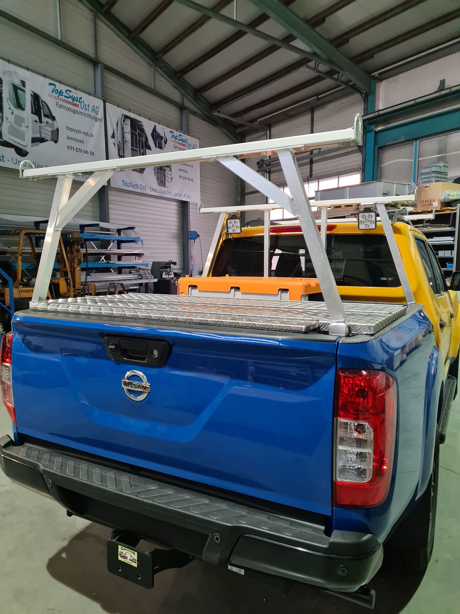 Blauer Nissan-Truck mit silbernem Gepäckträger und einer gelben Aufbewahrungsbox.
