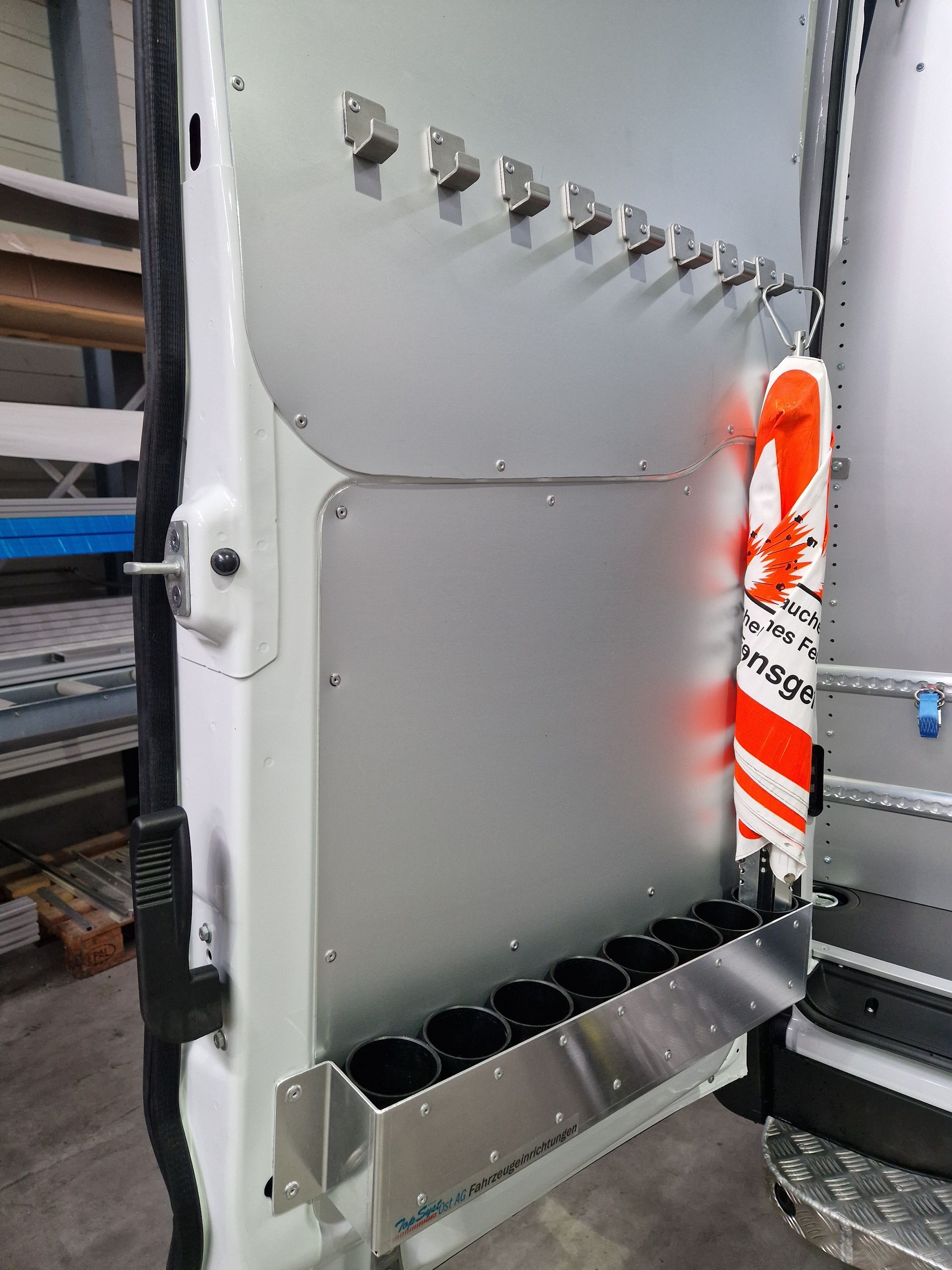 Innenseite einer weißen Lieferwagentür mit Metallverkleidung zur Werkzeugaufbewahrung; mit Haken, Haltern und Sicherheitsausrüstung.