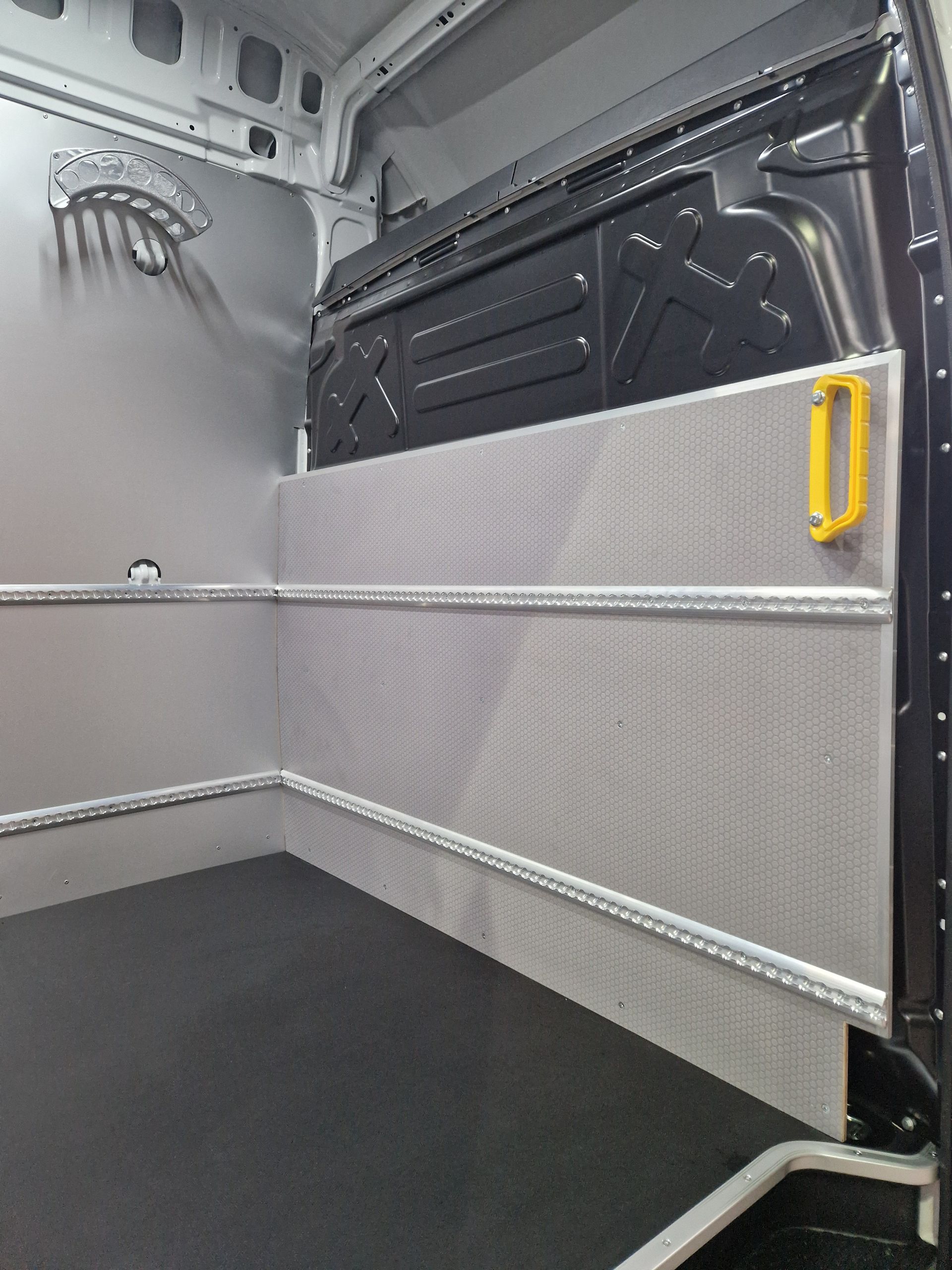 Innenraum eines Lieferwagens mit Metallwänden, schwarzem Boden und gelbem Griff.