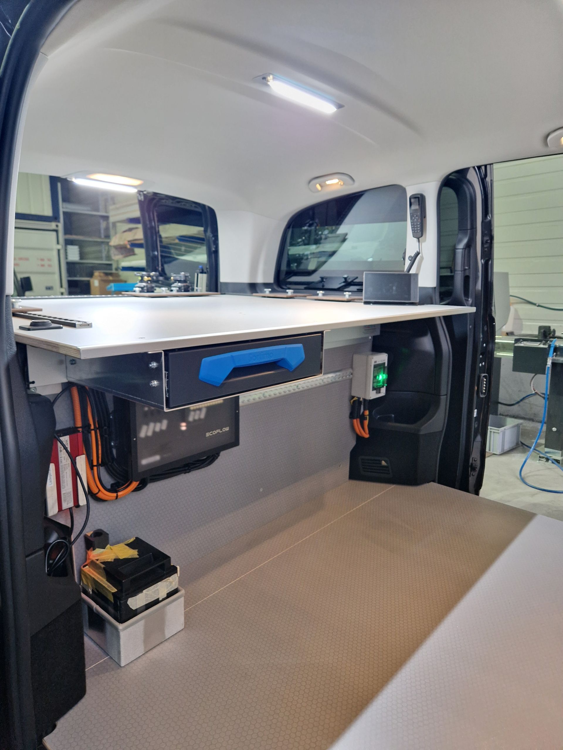 Innenansicht eines in einen mobilen Arbeitsplatz umgebauten Lieferwagens mit Schreibtisch, Wechselrichter und Ausrüstung.