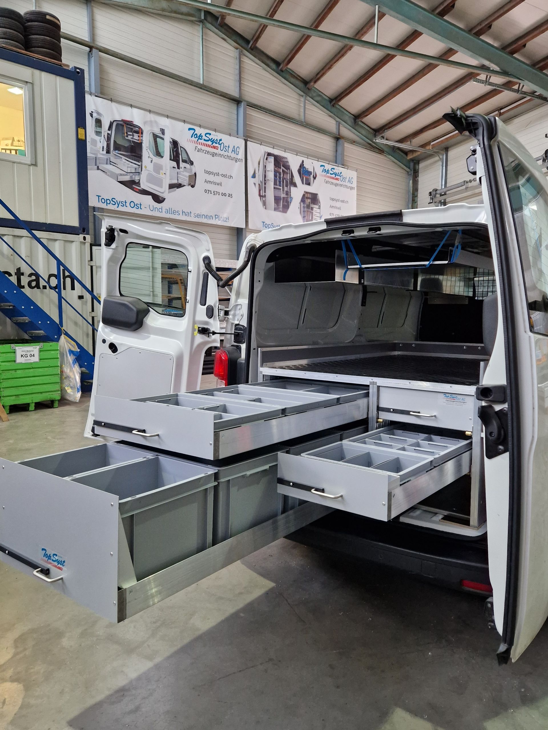 Weißer Lieferwagen mit offenen Hecktüren und ausziehbaren Schubladen voller Fächer in einer Werkstatt.