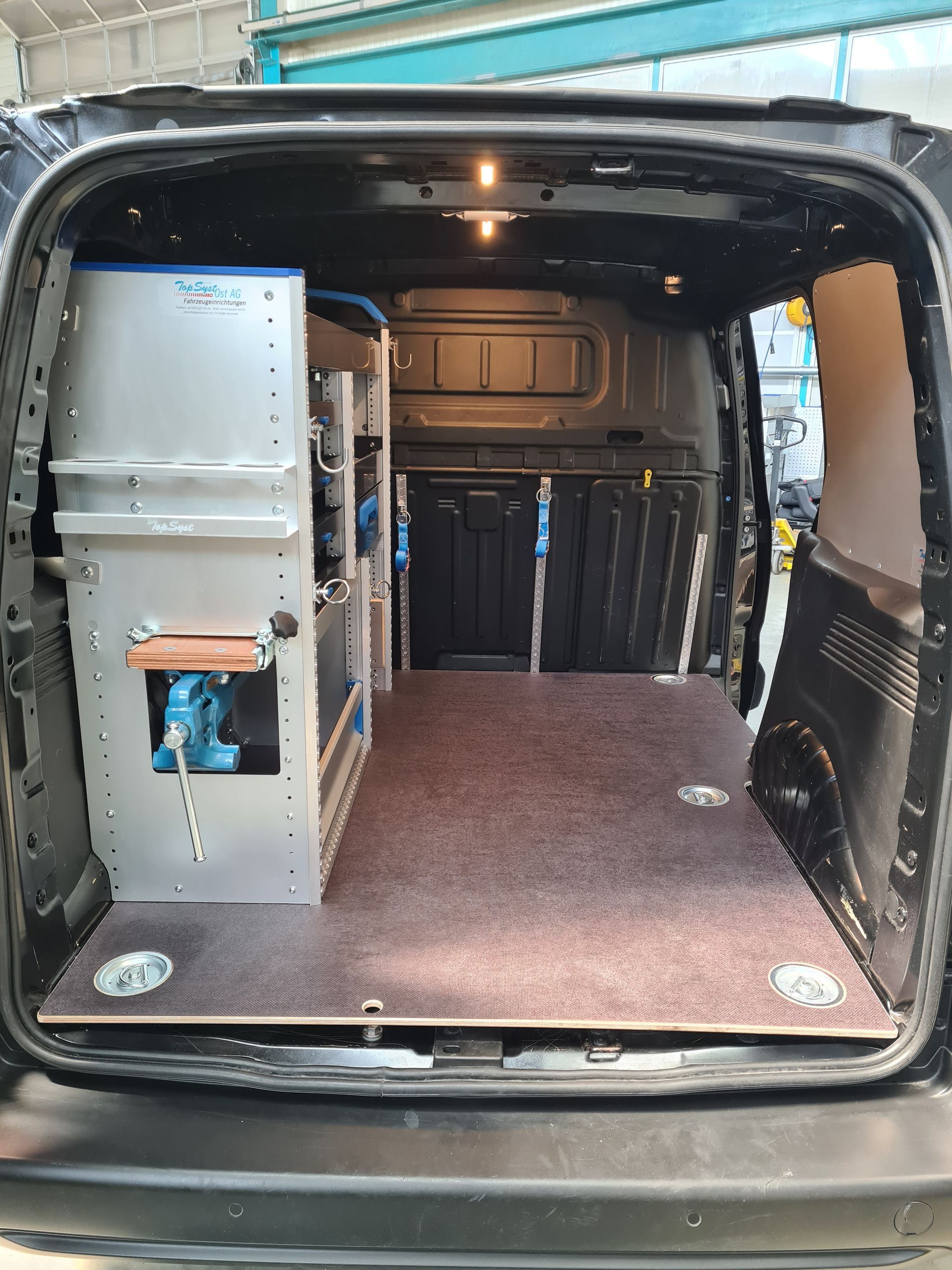 Im Inneren eines schwarzen Lieferwagens sind ein Werkzeugschrank aus Metall und ein Holzboden zu sehen.