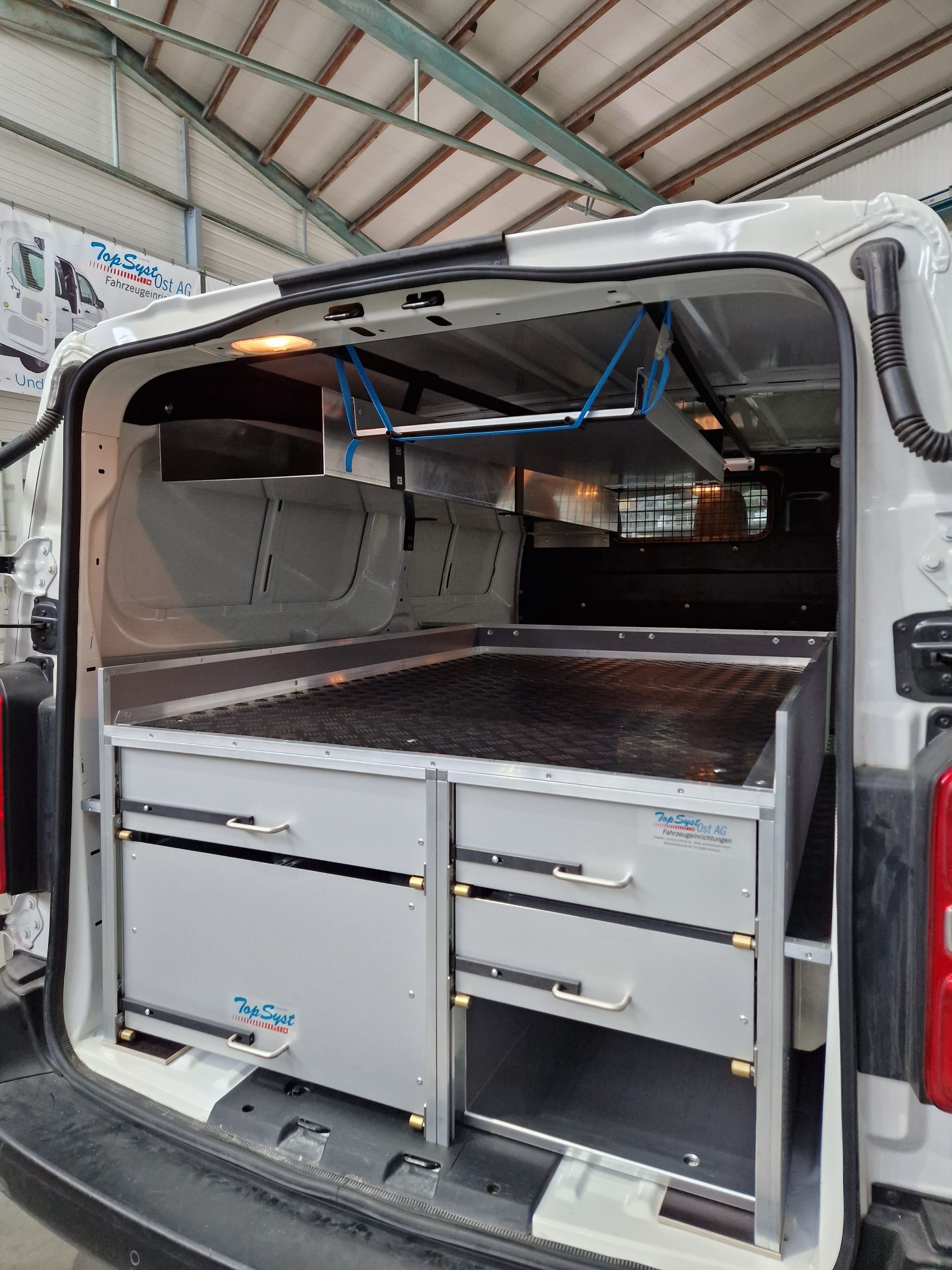 Weißer Van-Innenraum mit grauen Metallschubladen und Dachregal.
