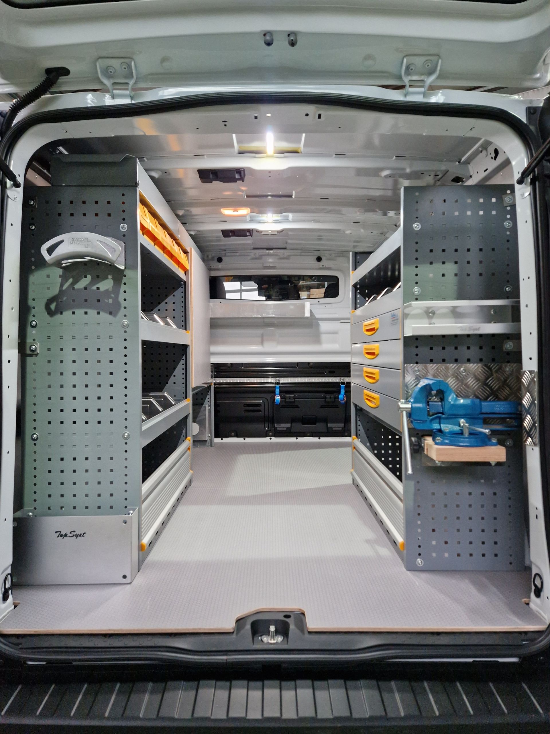 Innenraum eines Lieferwagens mit maßgefertigten Regalen und Werkzeugaufbewahrung, beleuchtet durch Deckenleuchten.