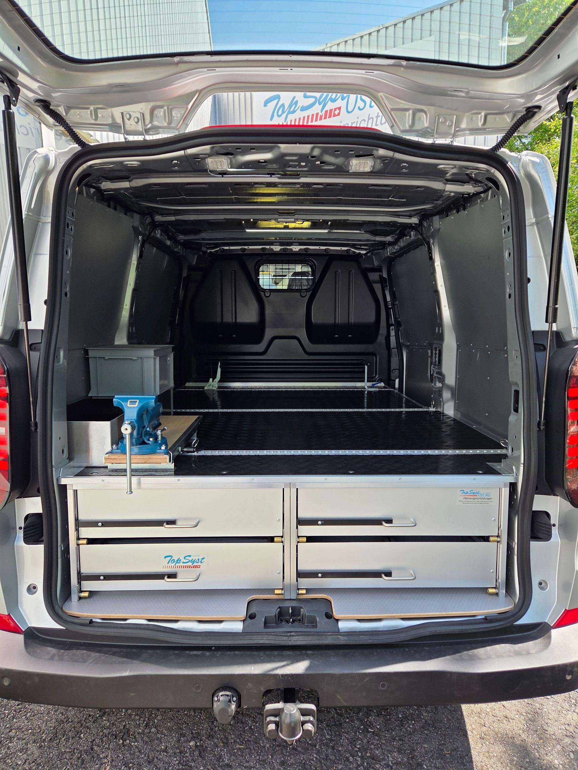 Innenraum eines grauen Lieferwagens, ausgestattet mit einer Werkbank und Schubladen.