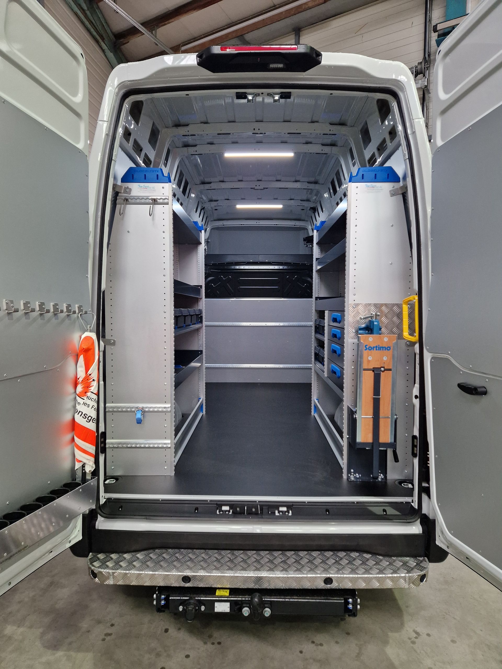Offener weißer Arbeitstransporterinnenraum mit Regalen, Werkzeugen und Beleuchtung.