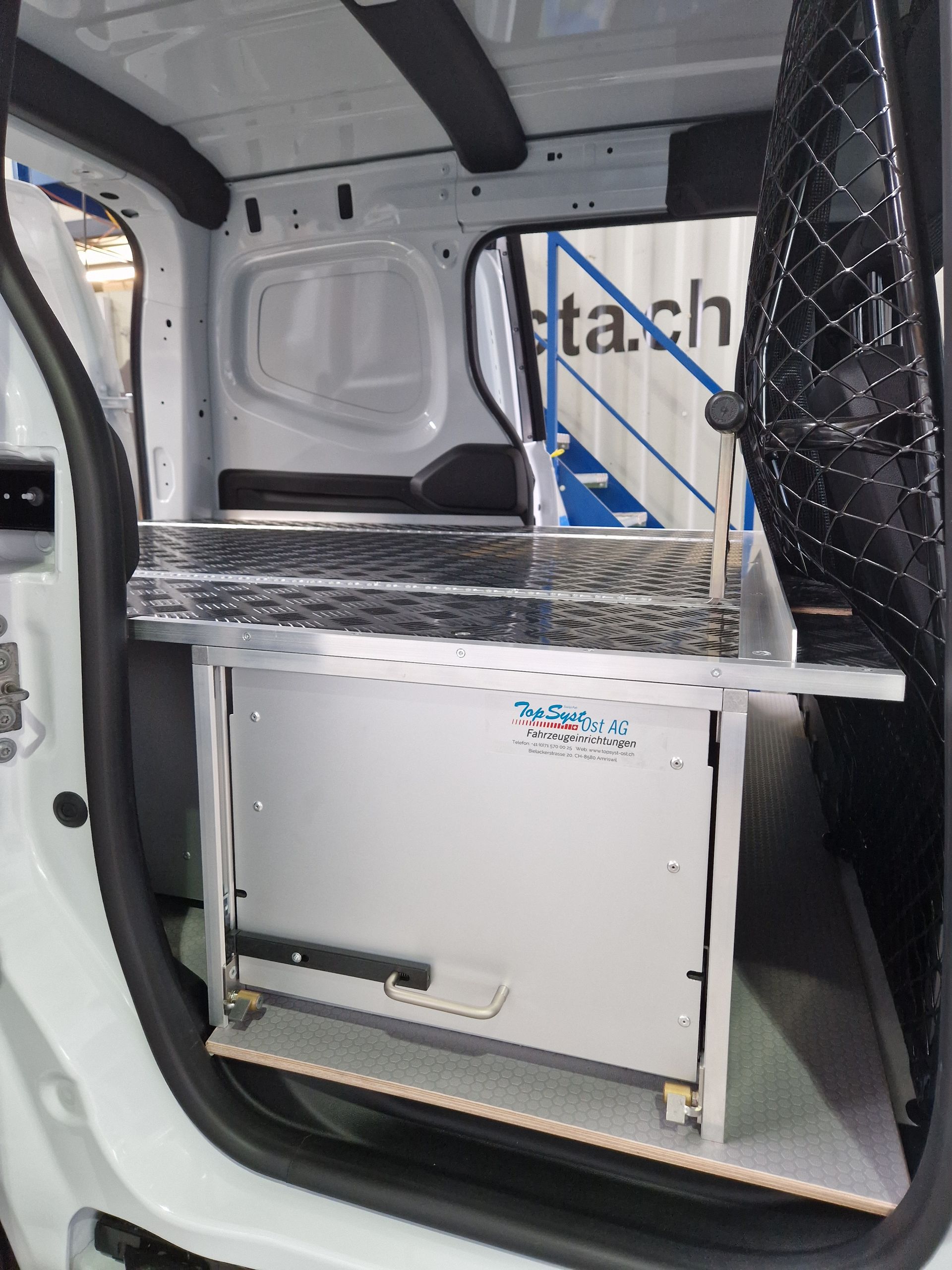 Seitenansicht des Innenraums eines Lieferwagens mit montierter Metallaufbewahrungseinheit und Sicherheitsnetz.