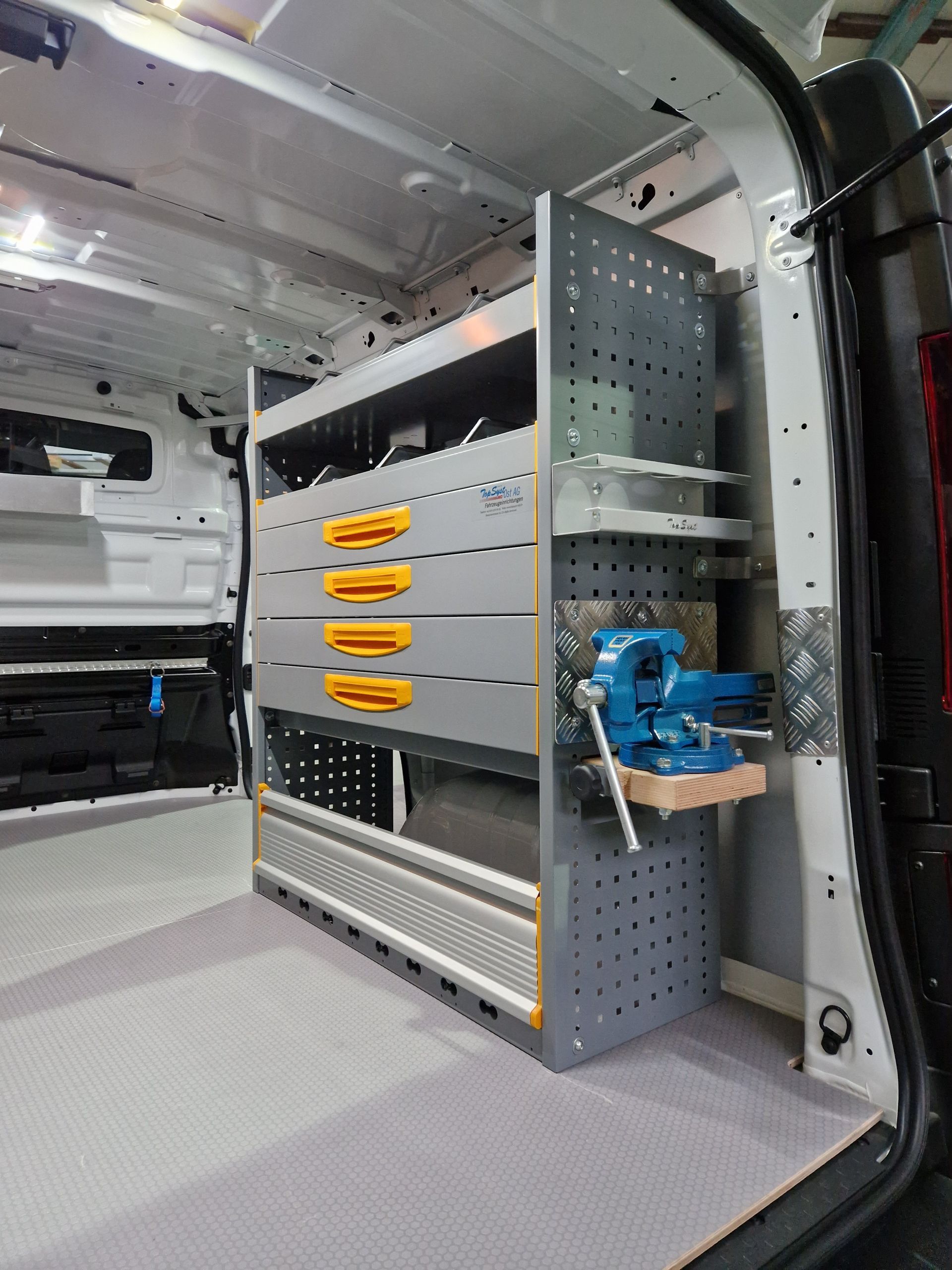 Innenraum eines Lieferwagens mit einem grau-gelben Werkzeugkasten und einem seitlich montierten Schraubstock.