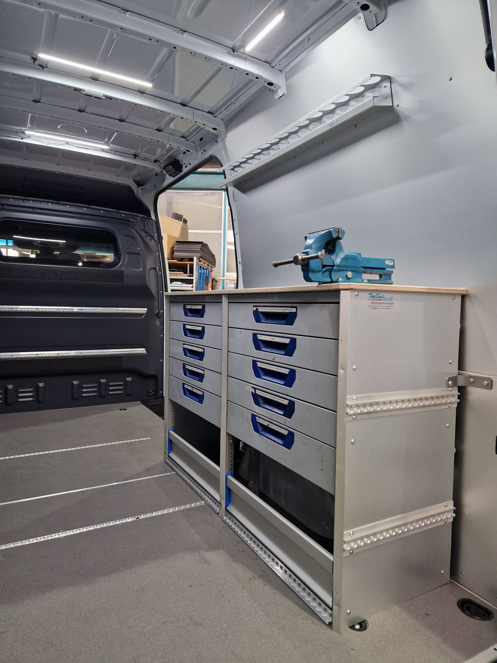 Im Inneren eines Lieferwagens steht ein grauer Metallschrank mit Schubladen und einem blauen Schraubstock darauf.