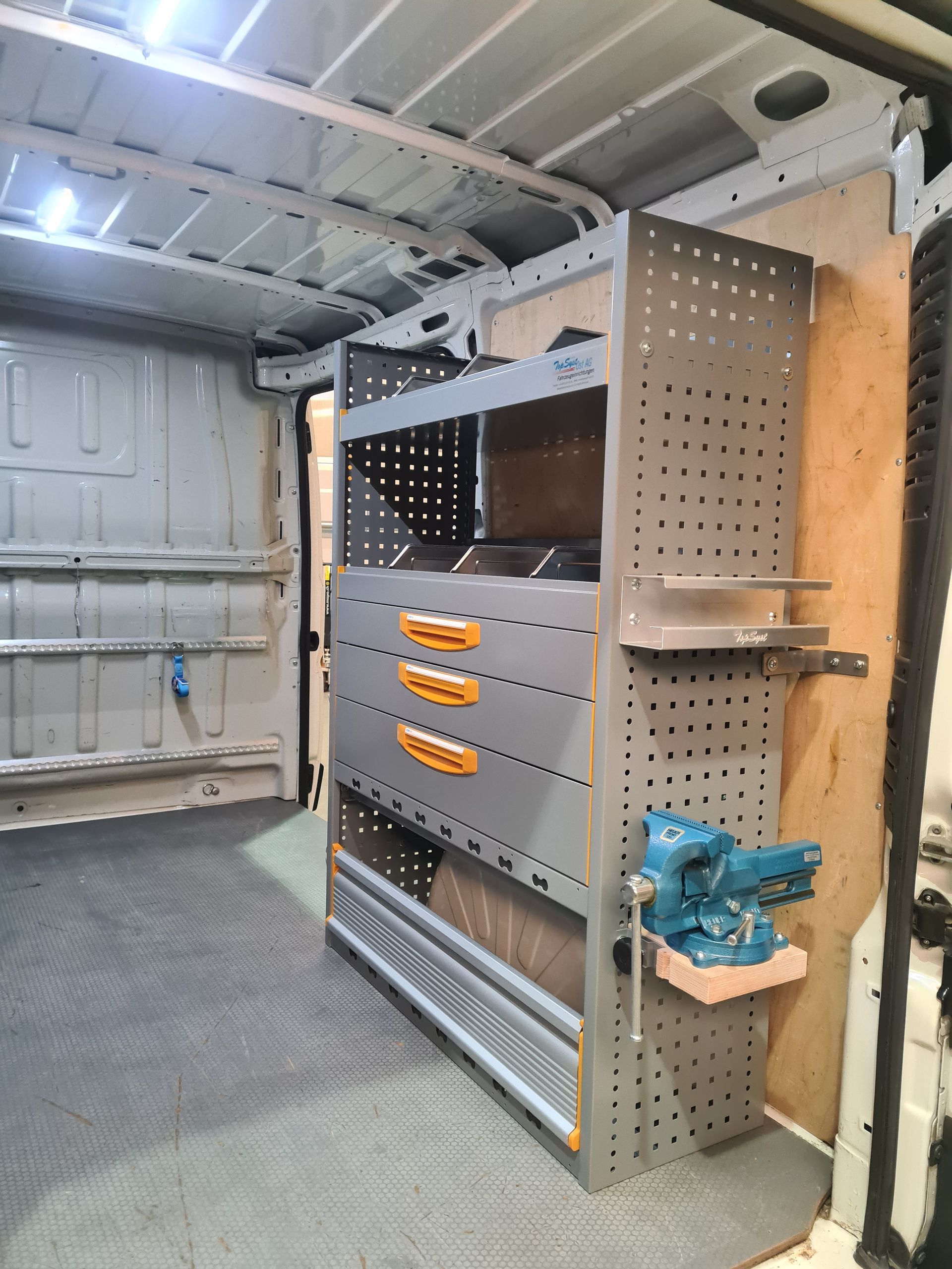 Innenraum eines Lieferwagens mit Regal, Schubladen und montiertem Schraubstock. Der Boden ist bedeckt.
