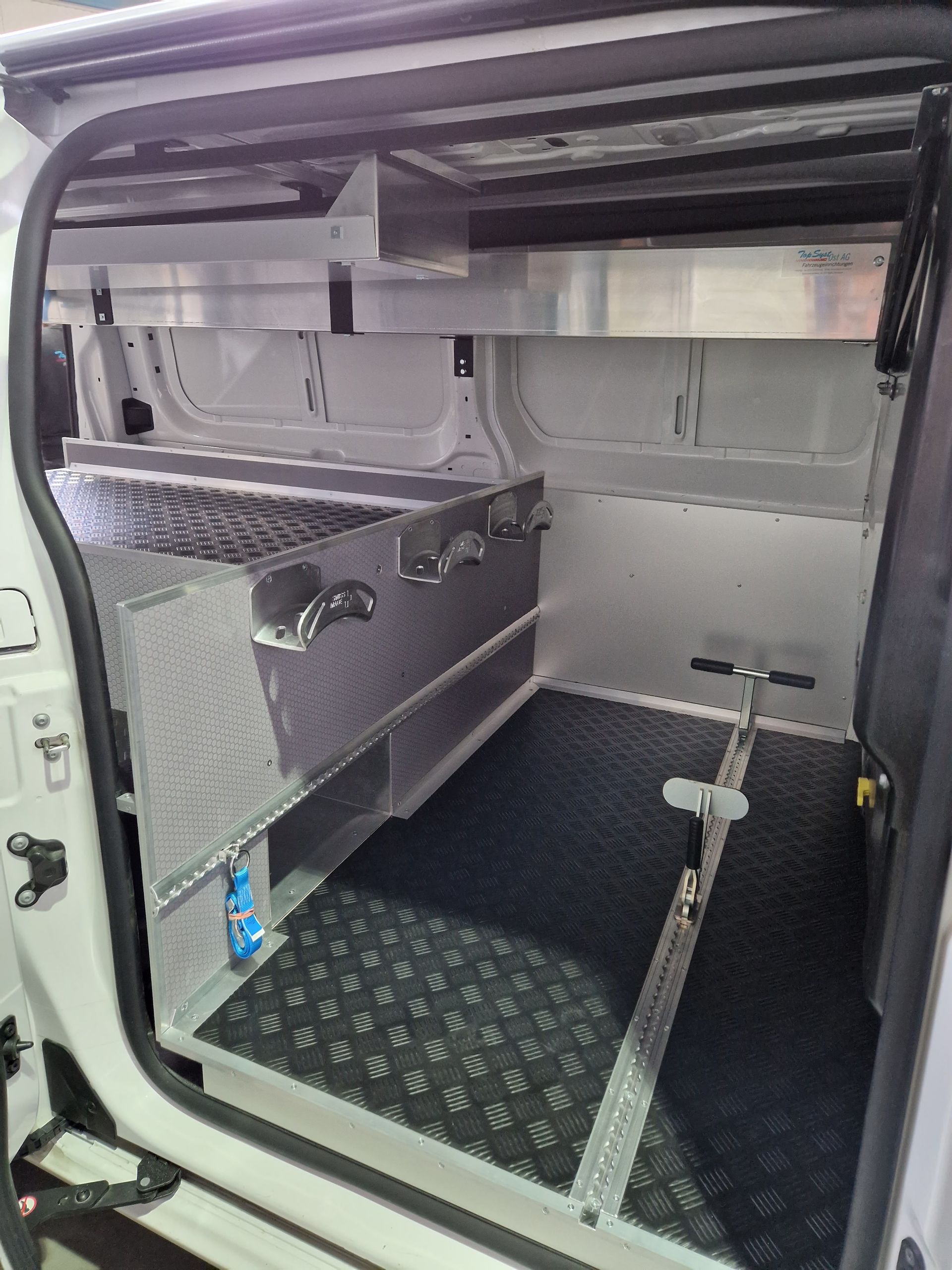 Innenraum eines weißen Lieferwagens mit maßgefertigten Metallregalen und Lagerräumen. Schwarzer Gummiboden.