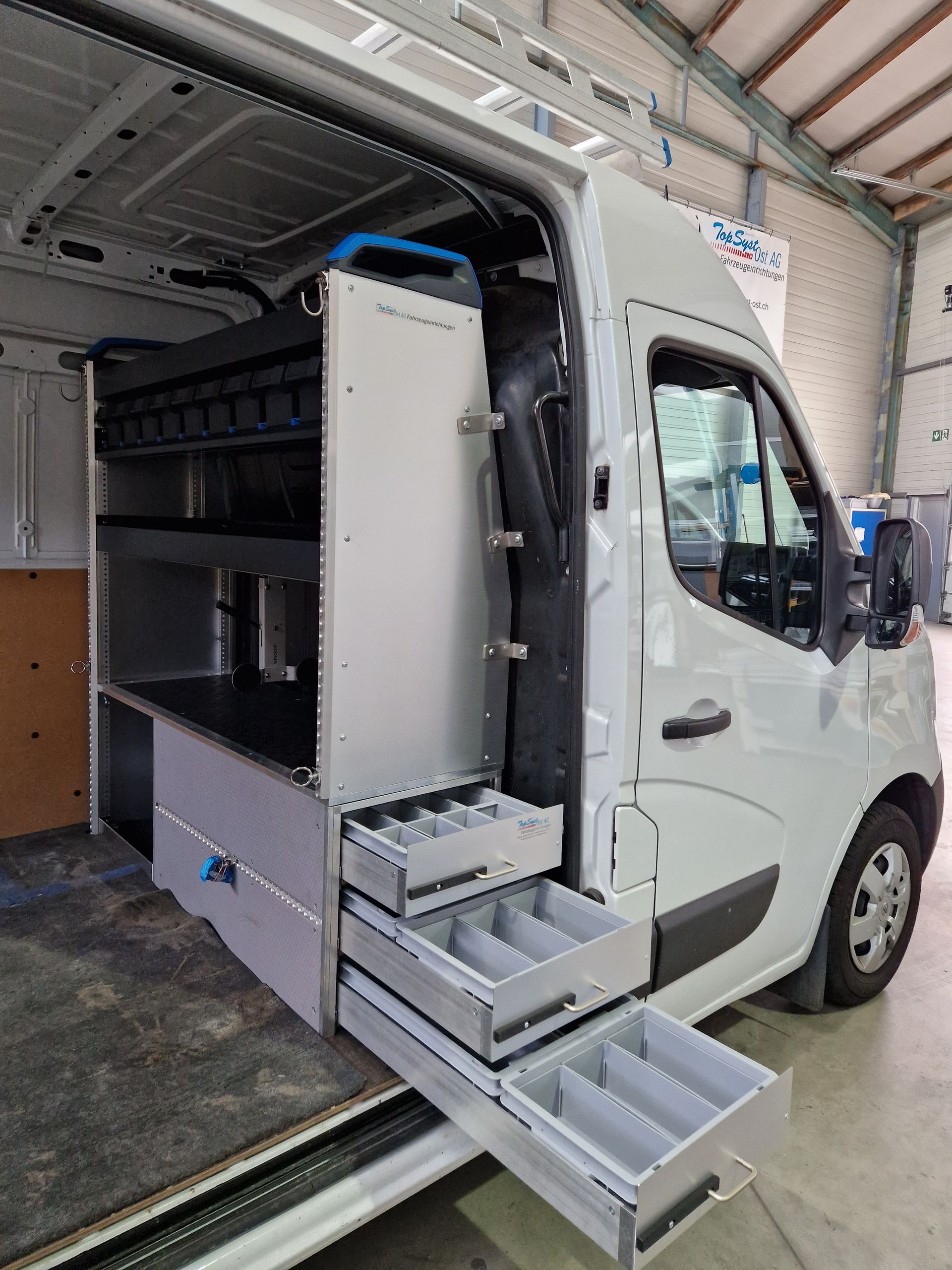 Innenraum eines weißen Arbeitstransporters mit Regalen, Schubladen und Werkzeugen.