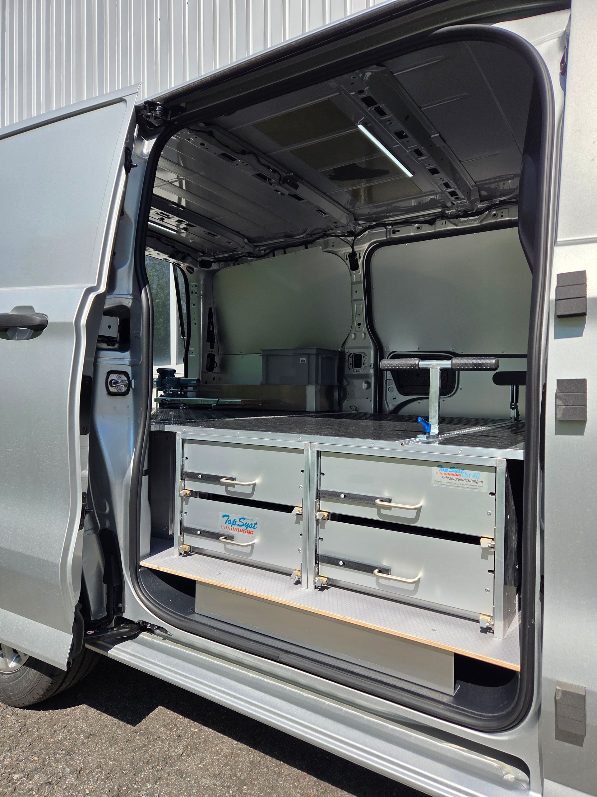 Silberner Van-Innenraum mit offener Seitentür, in dem Schubladen, Arbeitsbereich und Ausrüstung präsentiert werden.