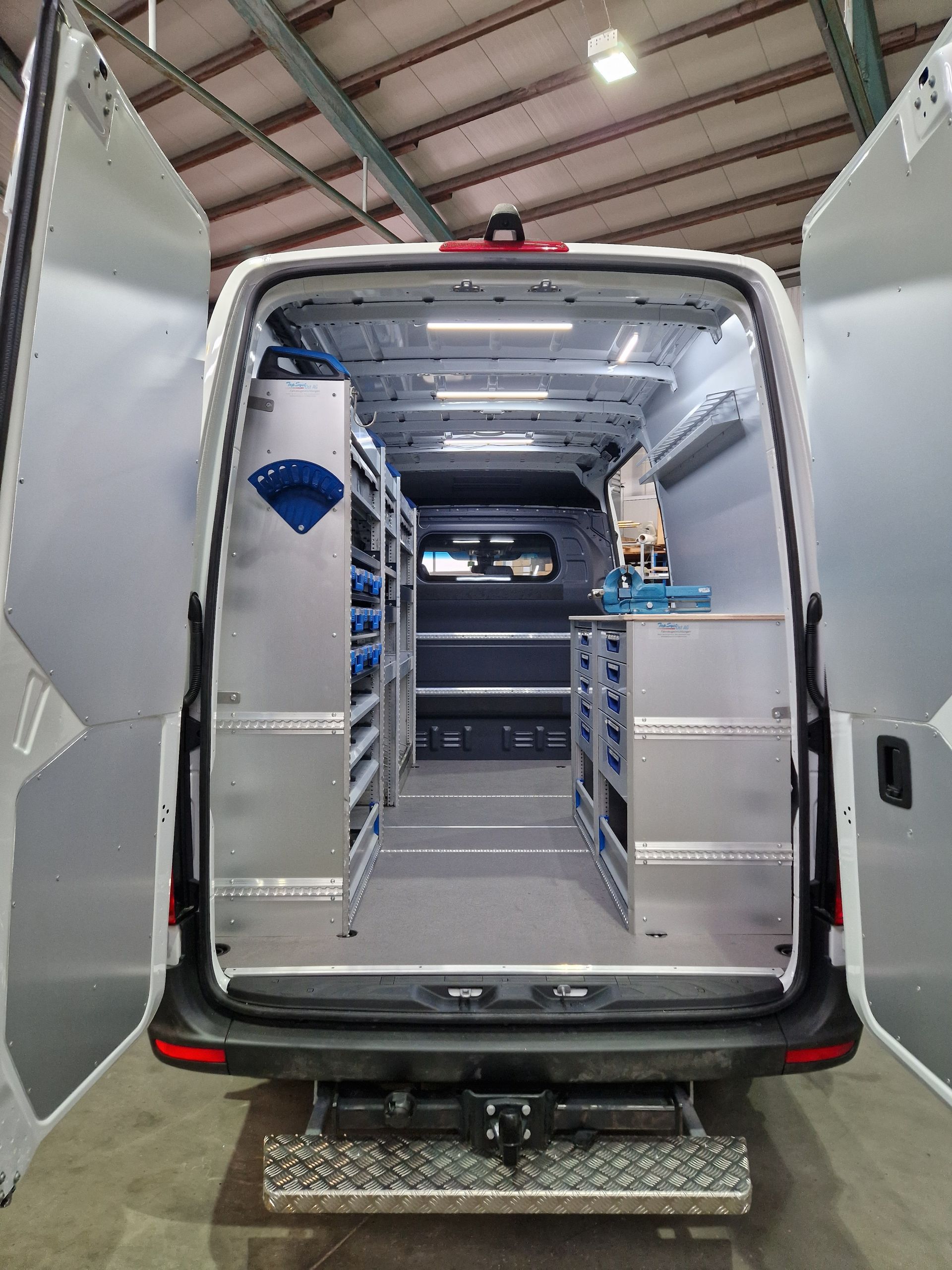 Rückseite eines weißen Lieferwagens mit offenen Türen, hinter denen sich geordnete Lagerregale und Schubladen befinden.