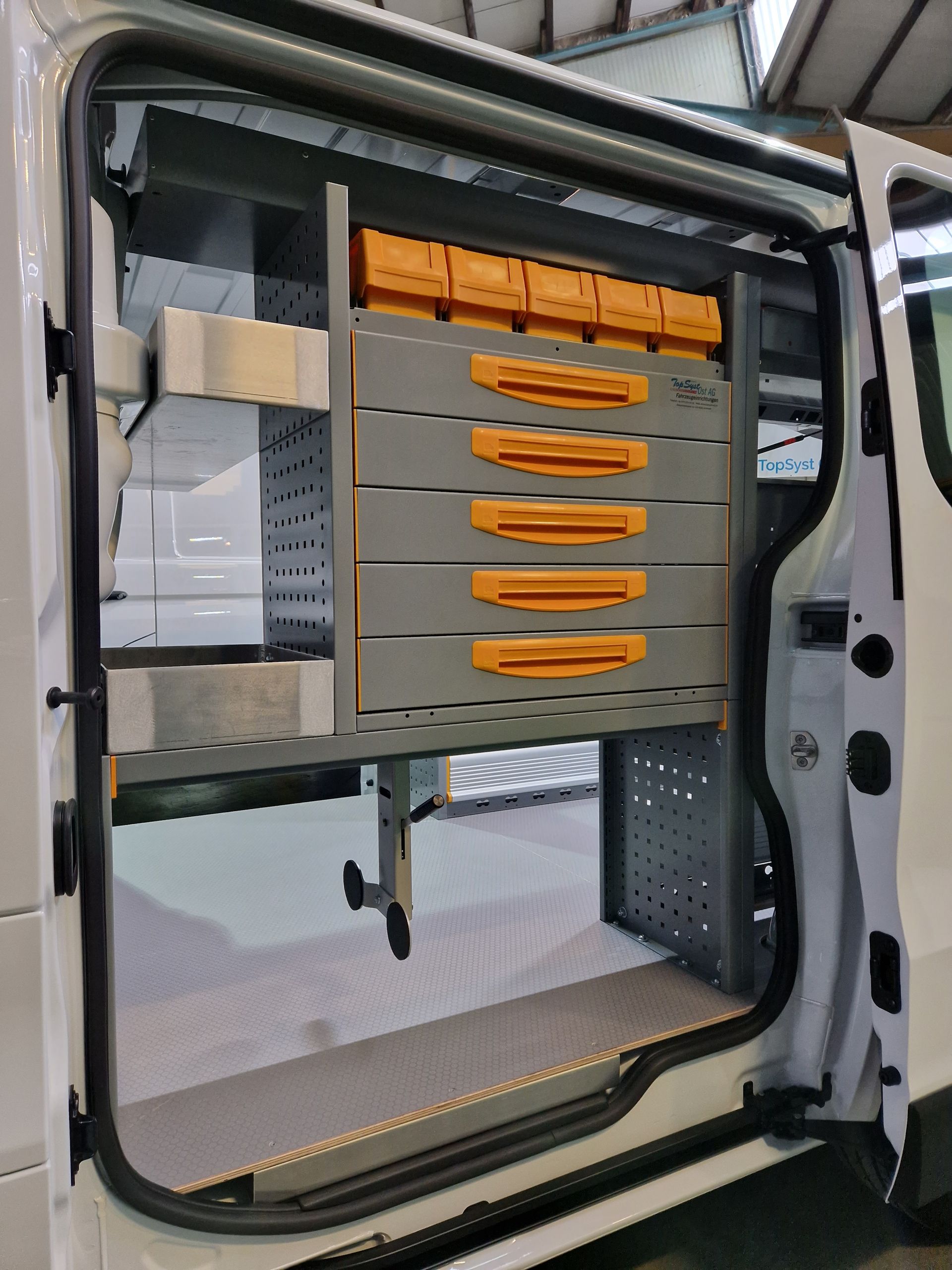 Weißer Van-Innenraum mit grauen Regalen, orangefarbenen Behältern und Schubladen.