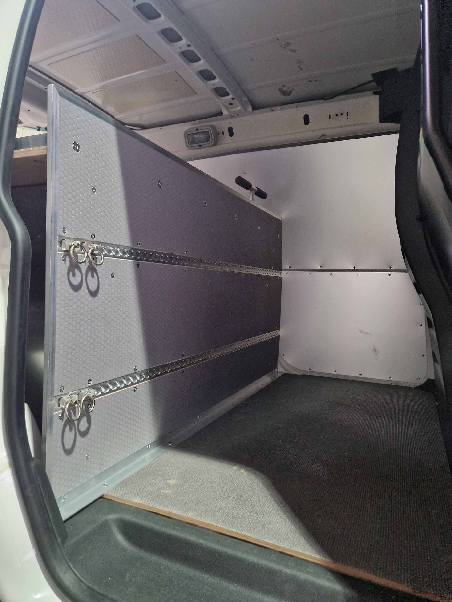 Innenraum eines Lieferwagens mit Regalen und Ketten, wahrscheinlich für Fracht. Grau und schwarz, leer.