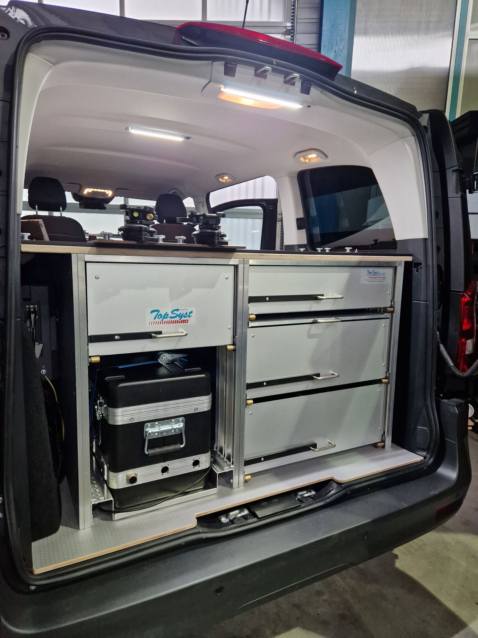 Offener Van-Innenraum mit umgebautem Wohnmobil, ausgestattet mit einer Schrankeinheit mit Schubladen und Geräten.
