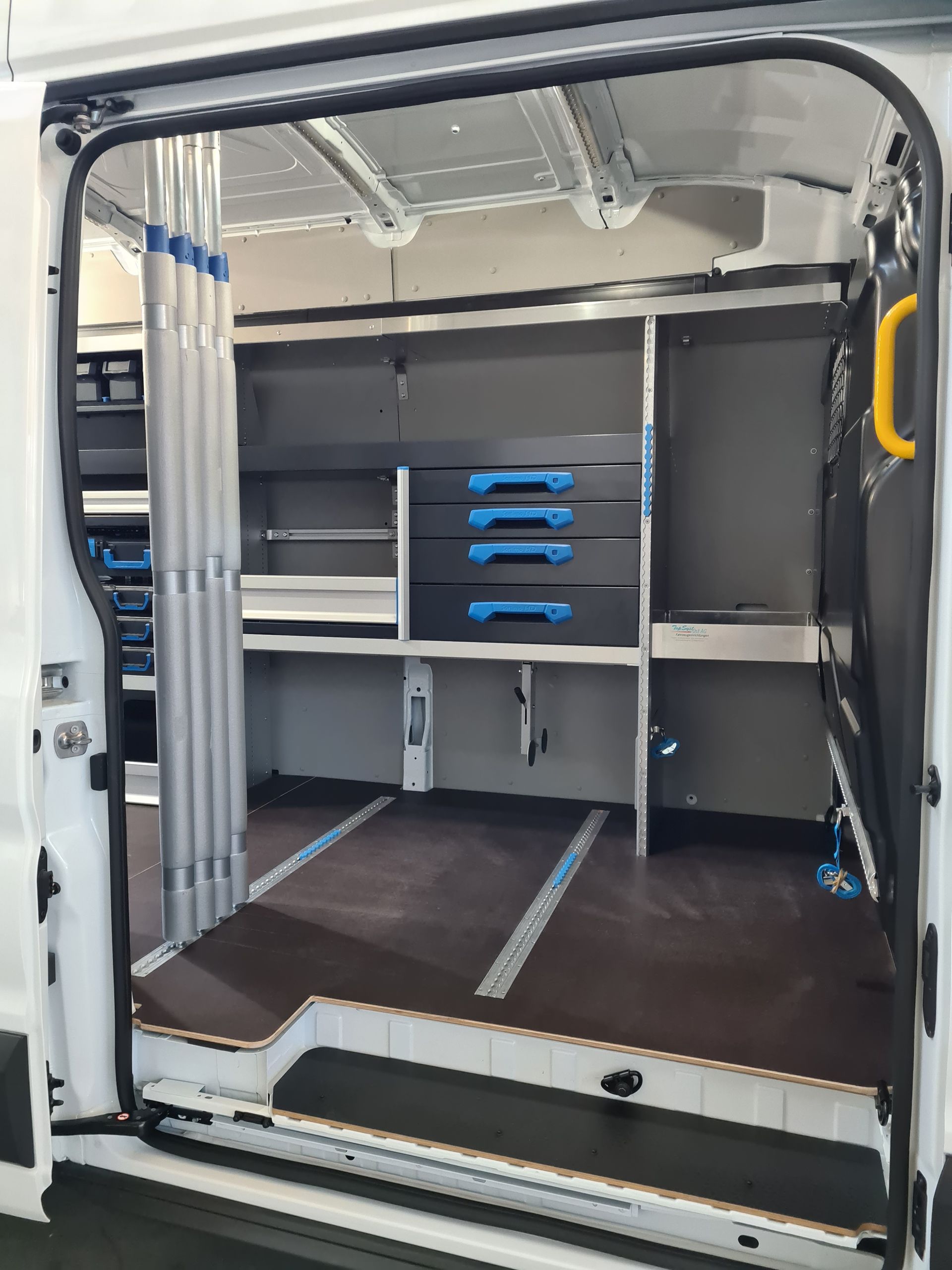 Innenansicht eines weißen Lieferwagens mit eingebauten Regalen, Schubladen und einer Klappleiter.