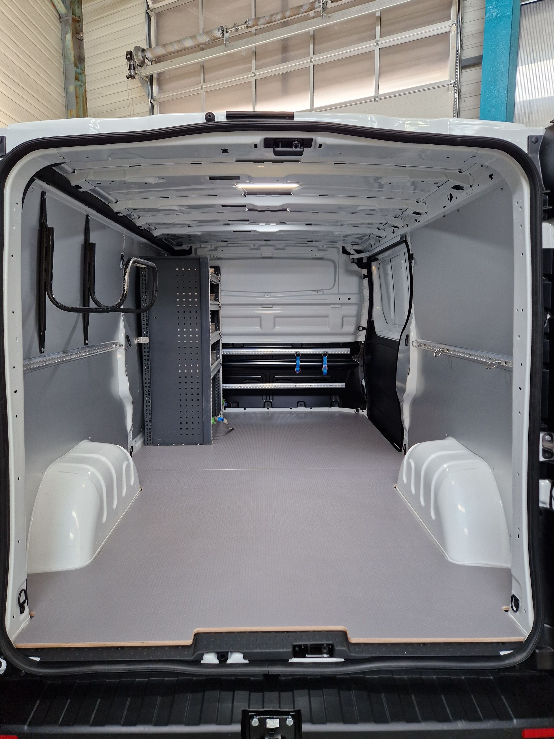 Innenansicht eines weißen Lieferwagens mit grauem Boden und Regalen, mit Blick durch die hinteren Türen.