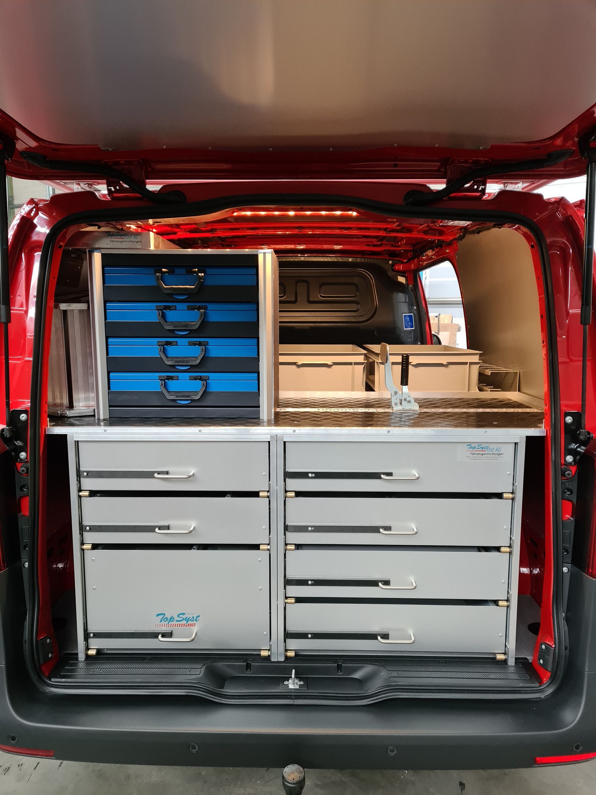 In einem roten Lieferwagen befindet sich eine organisierte Werkzeugaufbewahrung mit blauen und silbernen Schubladen.