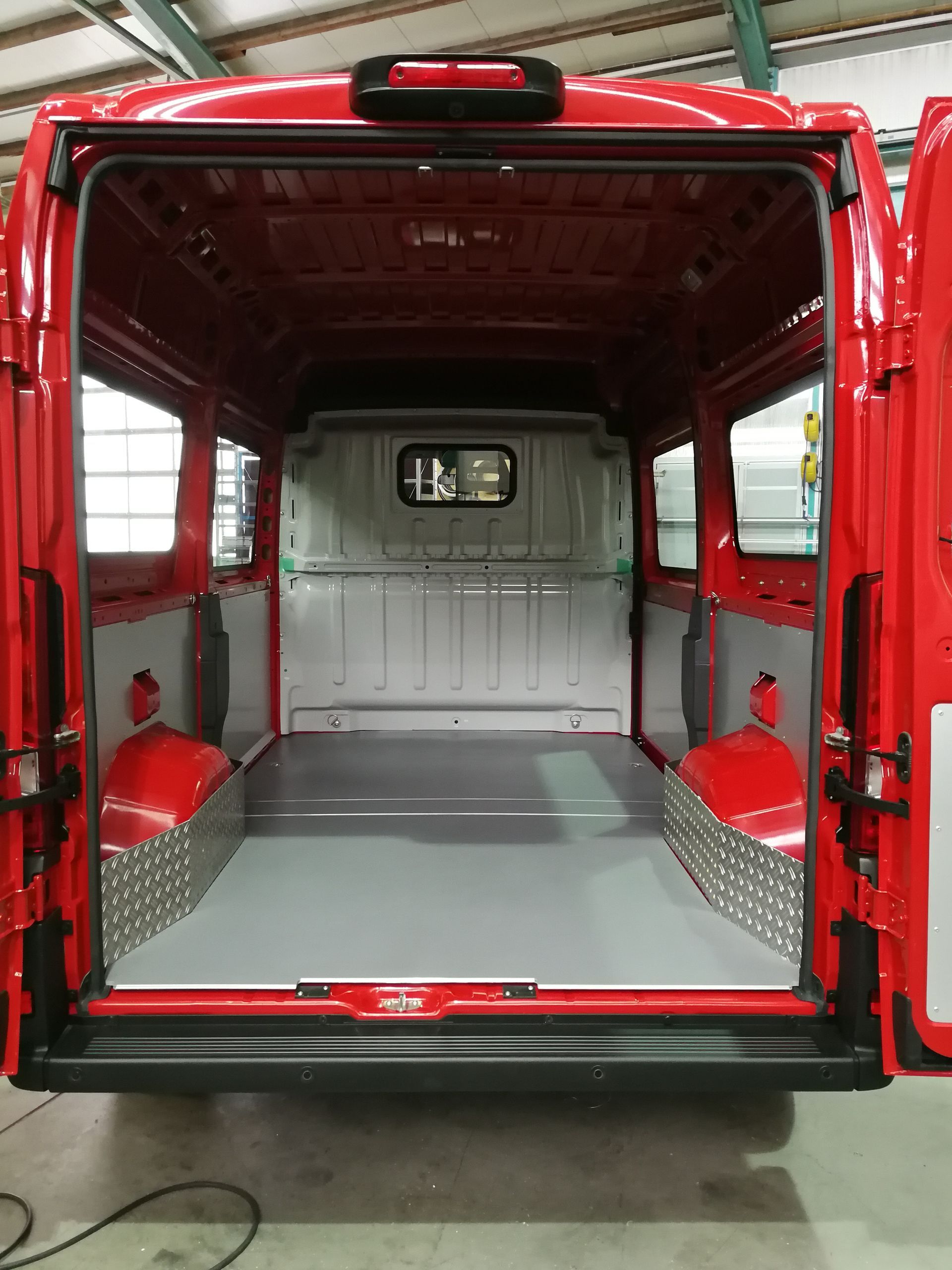Innenraum des roten Lieferwagens, leerer Laderaum, grauer Boden, Seitenwände aus Riffelblech, offene Türen.