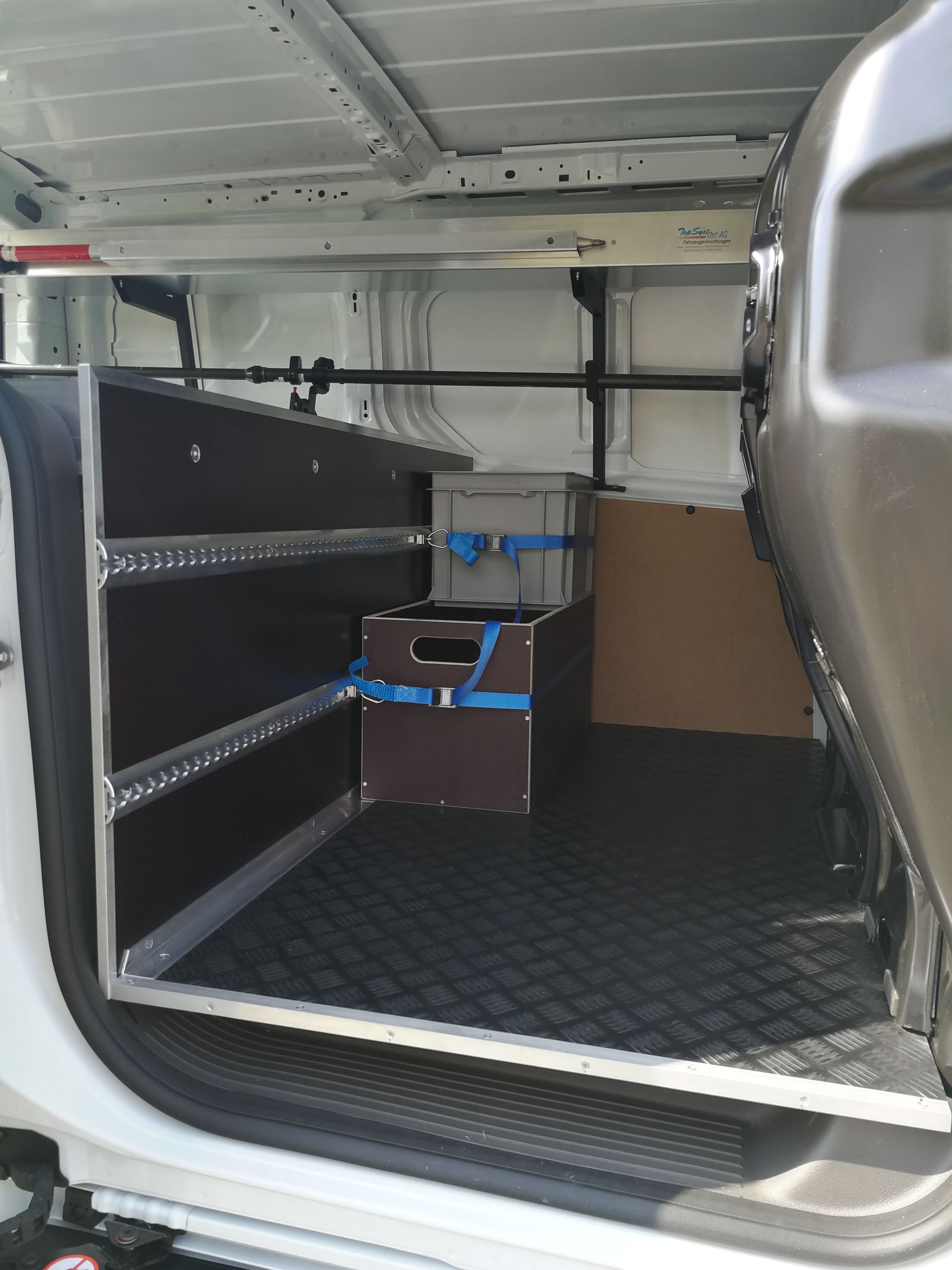 Innenraum eines weißen Lieferwagens mit maßgefertigten Regalen und einer gesicherten Aufbewahrungsbox. Schwarzer Gummiboden und grauer Metallrahmen.