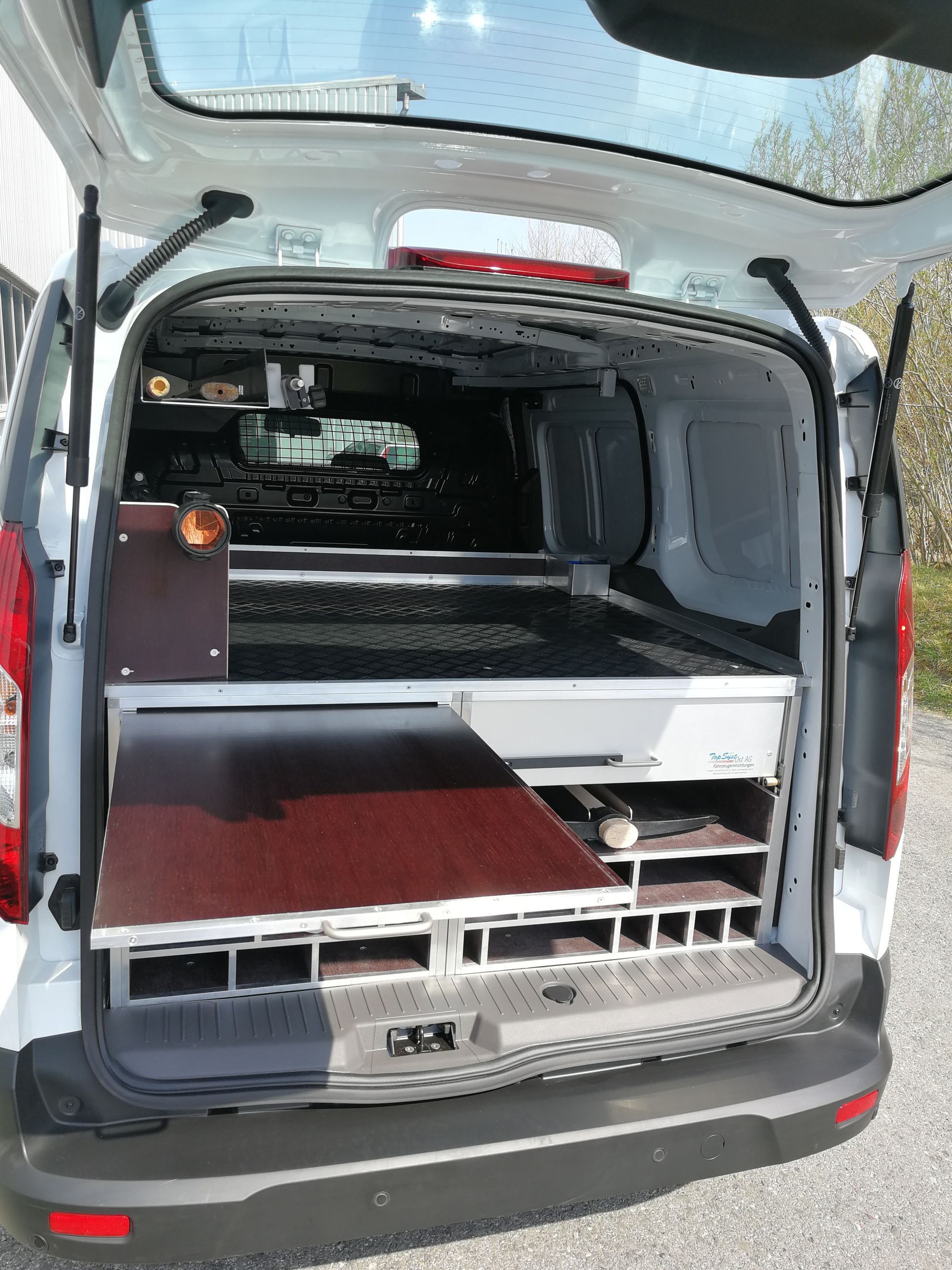 Offener weißer Van-Innenraum mit eingebauten Holzregalen und Staufächern.