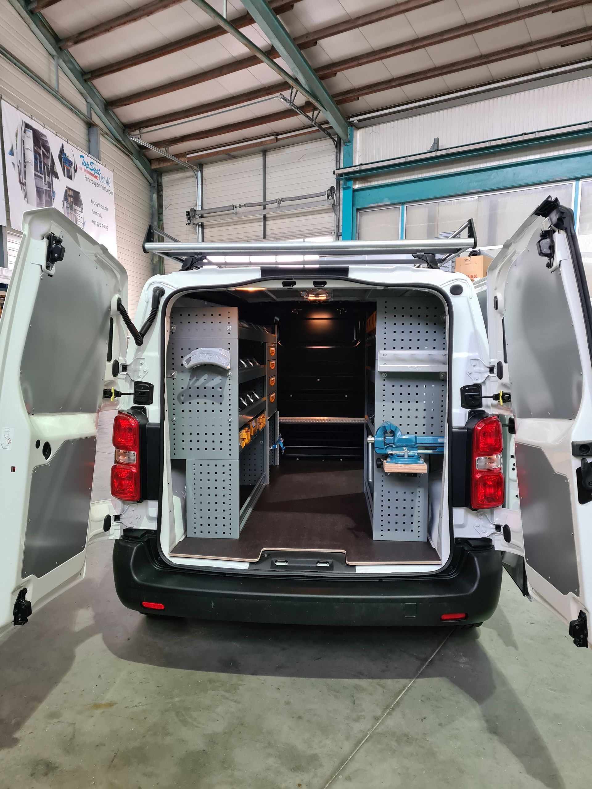 Weißer Lieferwagen mit offenen Türen, in dessen Inneren geordnete Regale und Werkzeuge zu sehen sind.