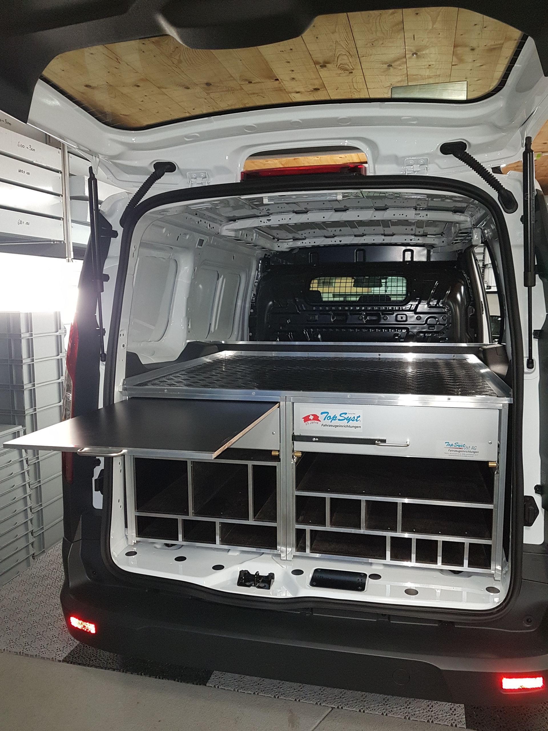 Weißer Van-Innenraum mit individuell angepassten Stau- und Arbeitsflächen. Offene Rückseite.