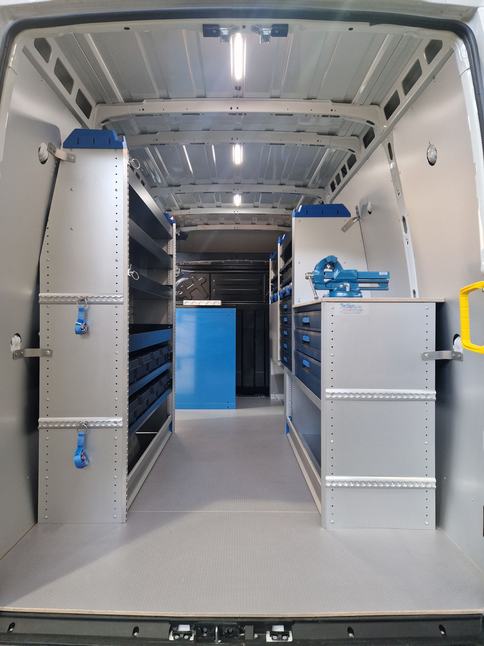 Innenraum eines Servicewagens mit Regalen, Schubladen und Werkzeugen. Graue und blaue Farben.