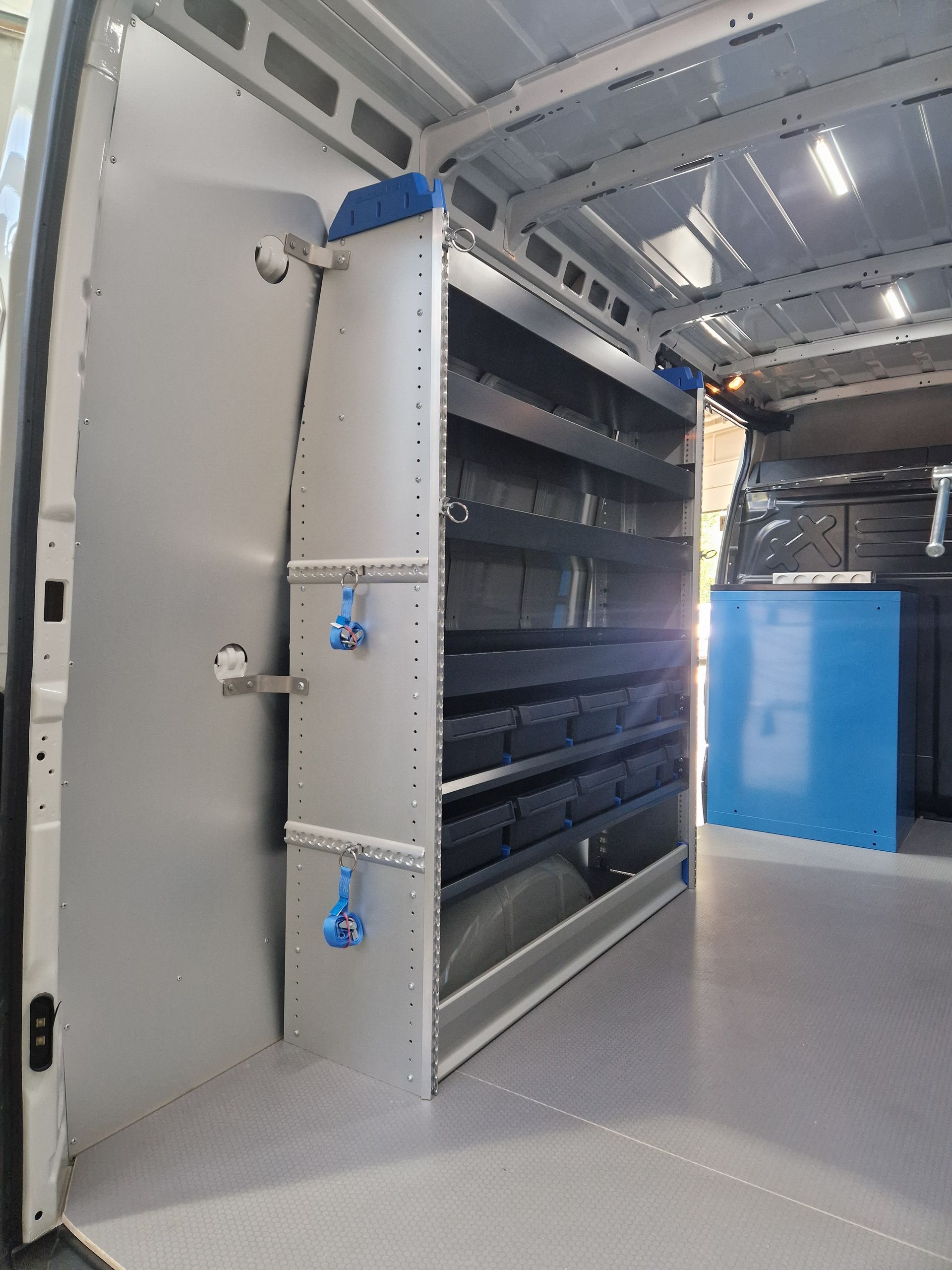 Innenraum eines Lieferwagens mit Regalen, Werkbank und Ladefläche. Graue und blaue Farben.