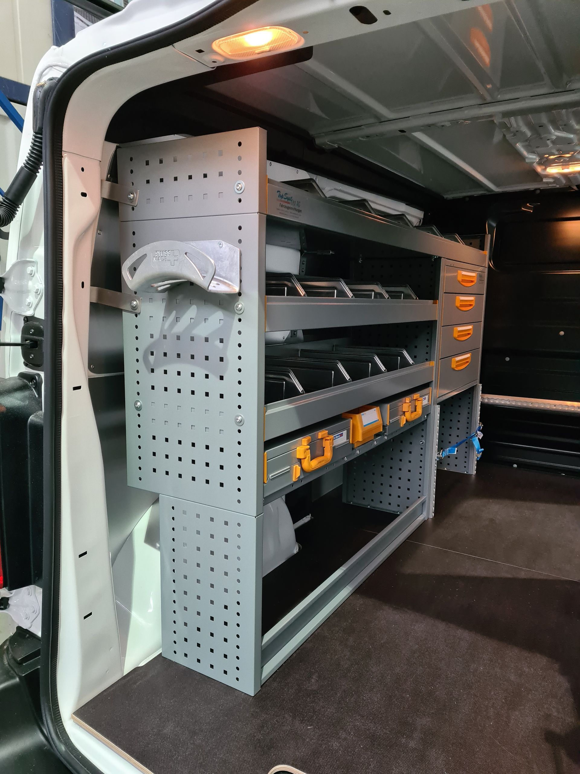 Innenraum eines Lieferwagens mit grauen Regalen, die Werkzeuge und Ausrüstung enthalten.