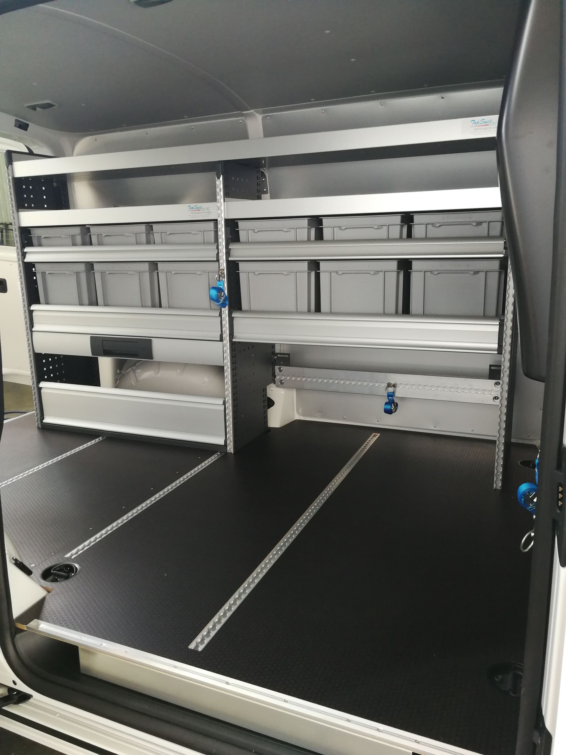 Innenraum eines Lieferwagens mit Regalen, Lagerbehältern und schwarzem Boden.