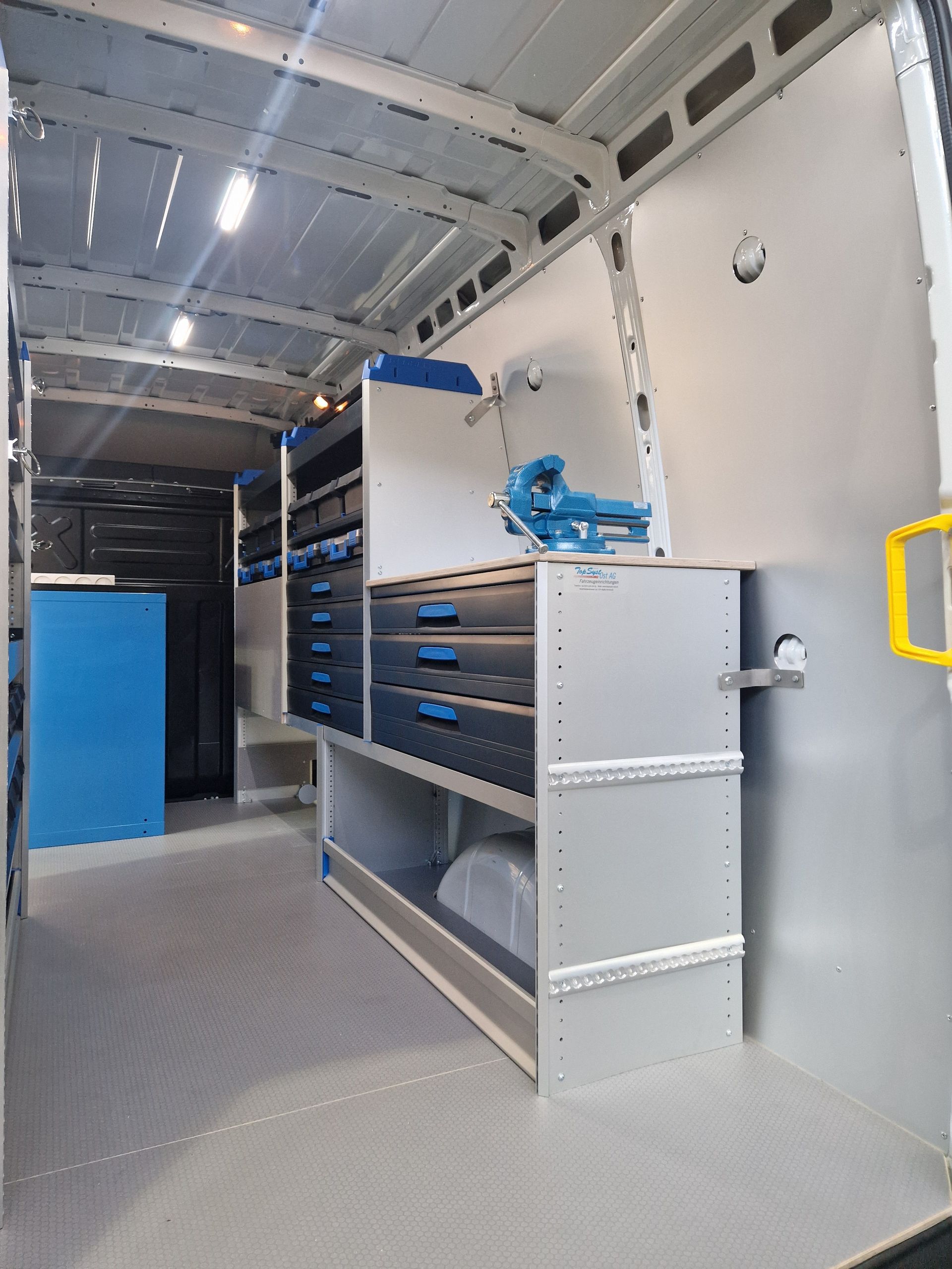 Innenansicht eines Lieferwagens mit grauem und blauem Werkzeugschrank und einer Werkbank.